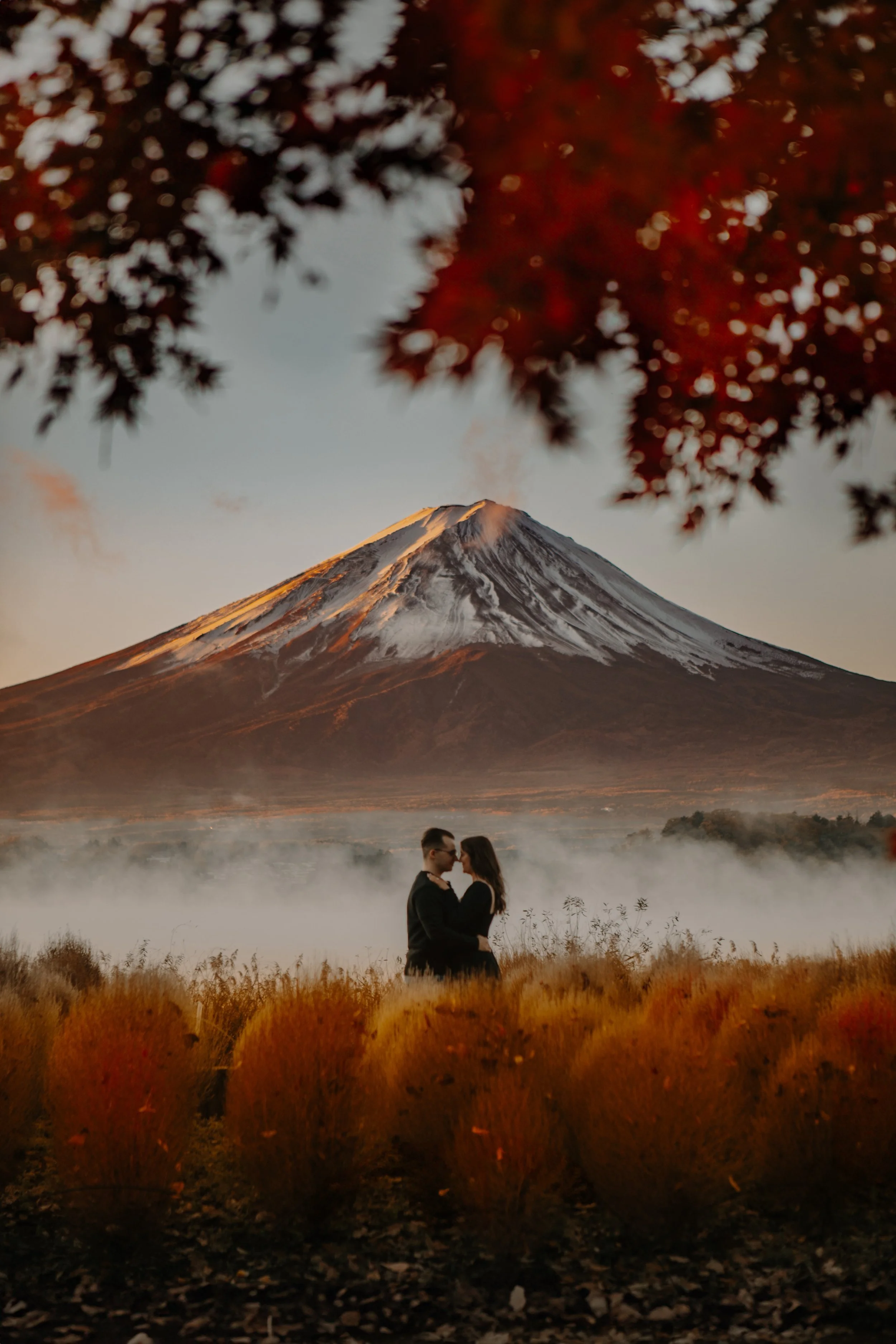 Couple embracing in golden morning mist near Lake Kawaguchiko with Mount Fuji at sunrise