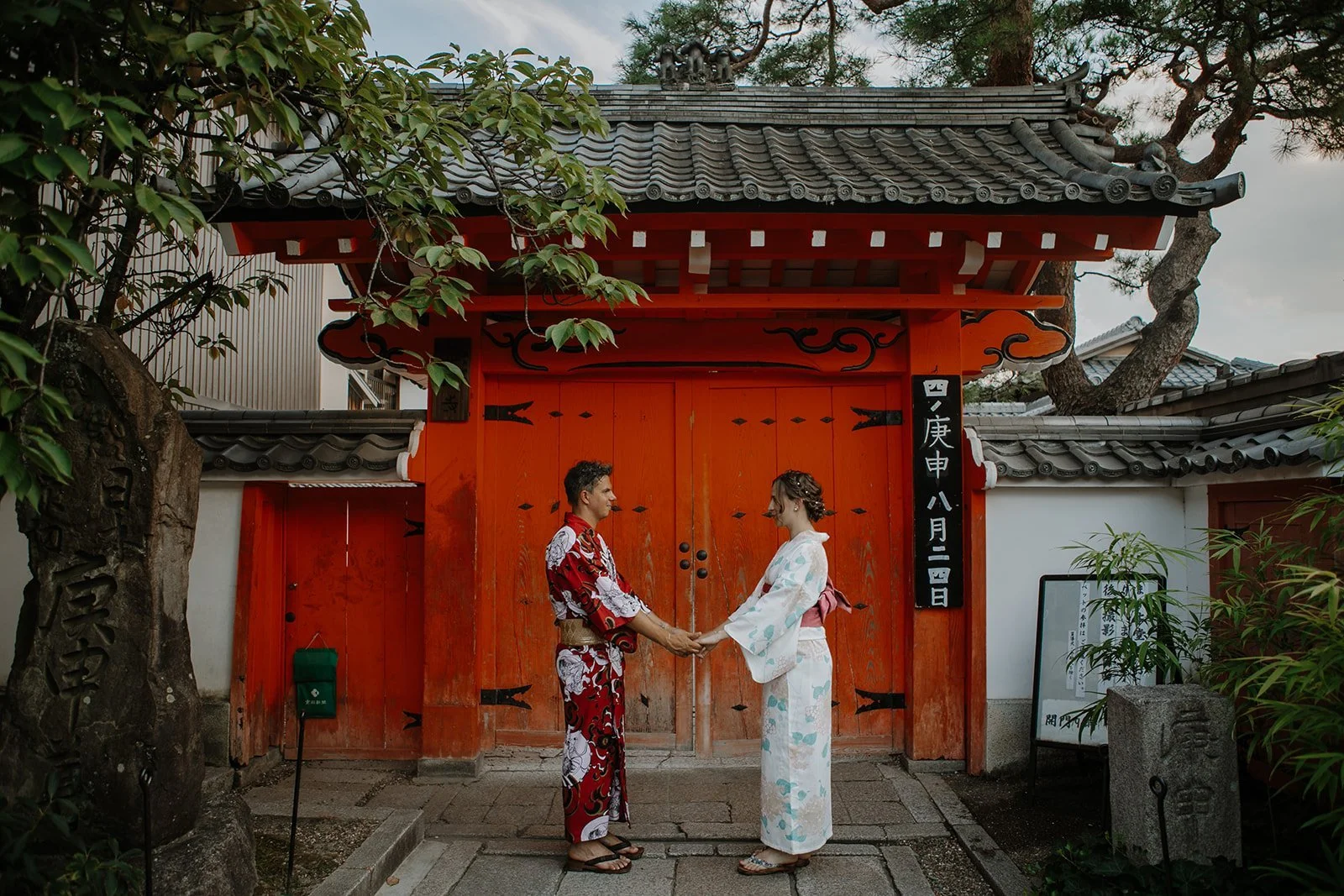 Couple in kimono holding hands in front of a vivid orange temple gate in Kyoto