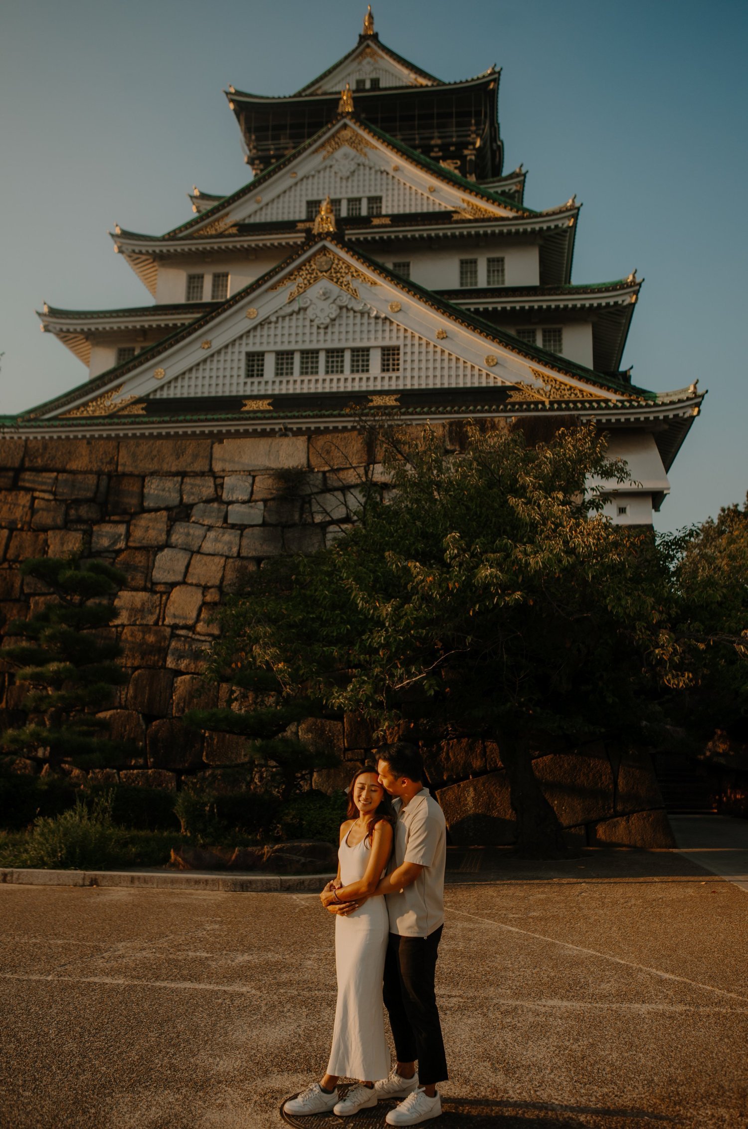 Couple embracing beside the stone walls of Osaka Castle at golden hour