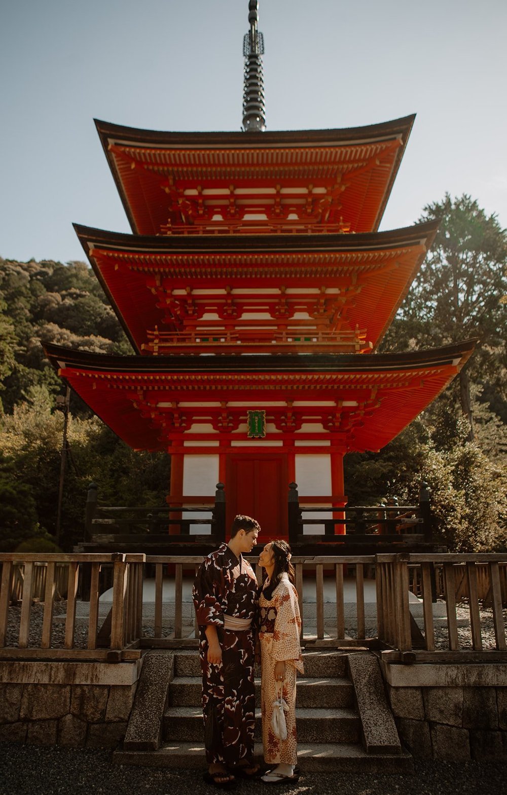 Couple in kimono facing each other in front of a three-story red pagoda in Kyoto, Japan