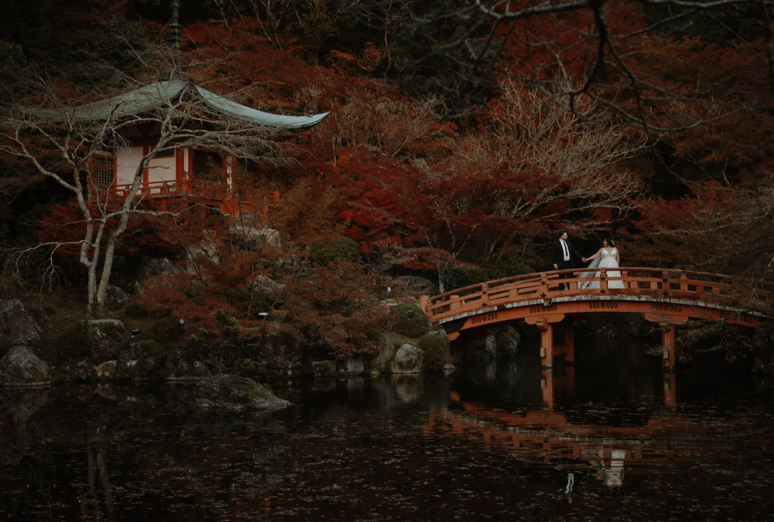 Bride and groom holding hands on the vermillion bridge at Daigo-ji temple during an autumn elopement in Kyoto, Japan