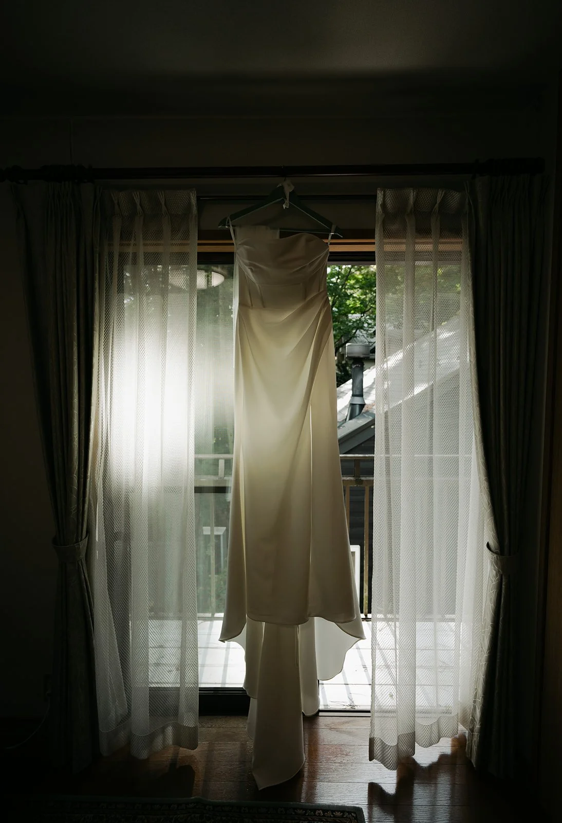 Strapless wedding gown hangs in a sunlit window ahead of the couple's Mount Fuji elopement ceremony.