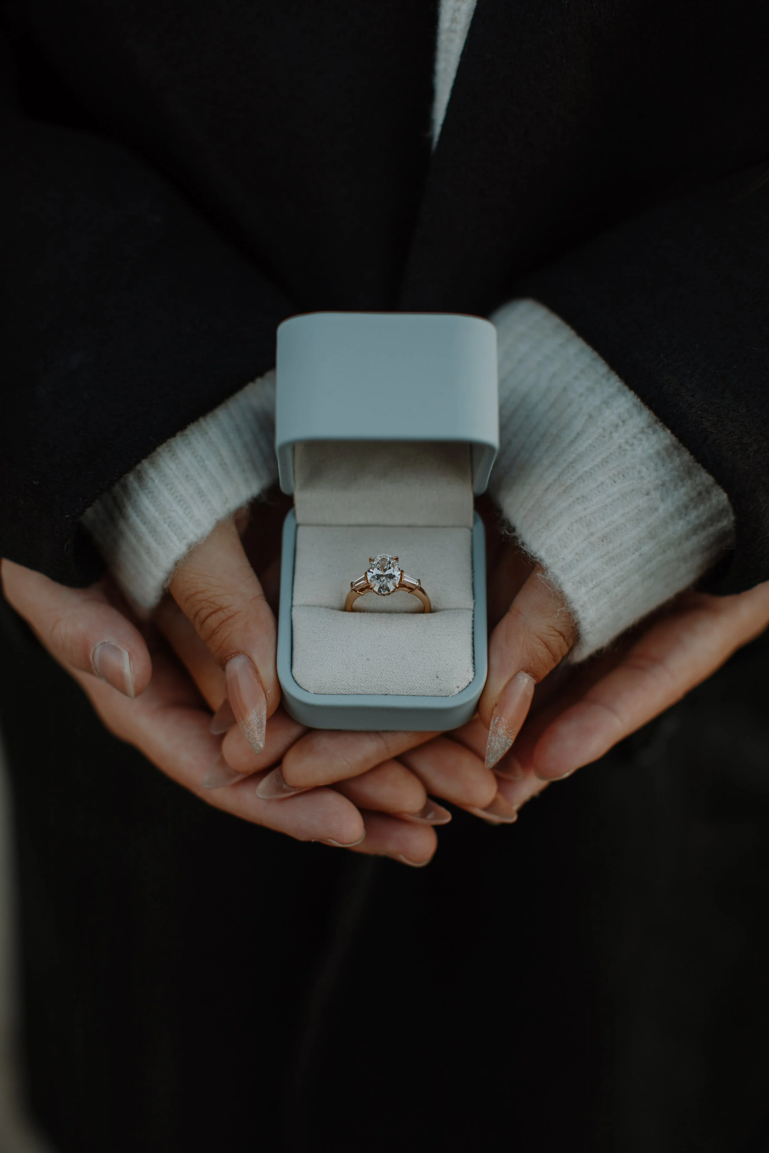 Close-up of hands holding an open ring box revealing a diamond engagement ring
