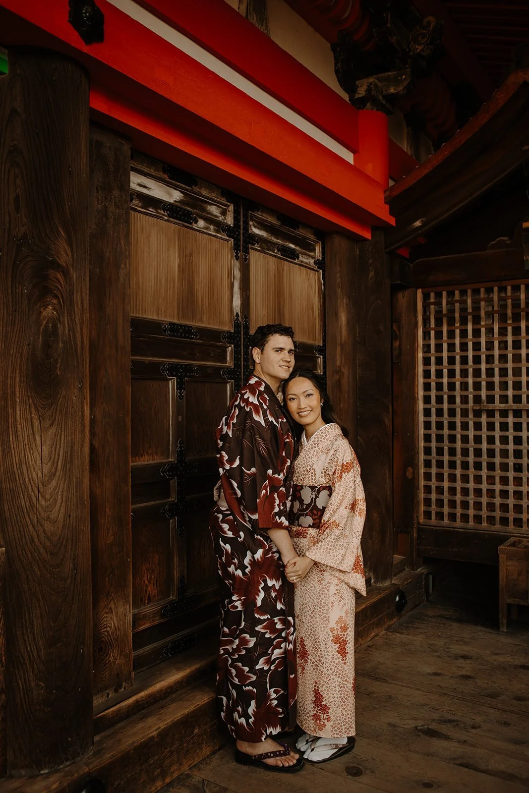 Couple in kimono standing together against a large wooden temple door in Kyoto, Japan