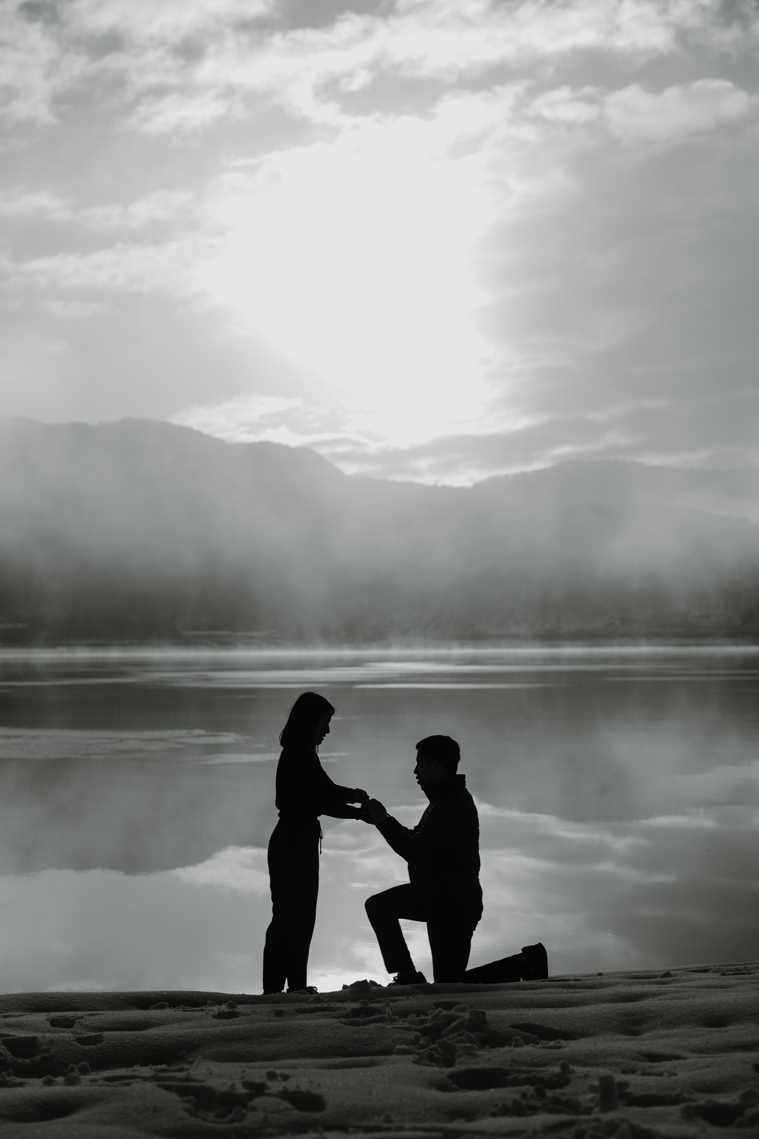 Black and white silhouette of a man kneeling to propose beside a misty lake near Mount Fuji