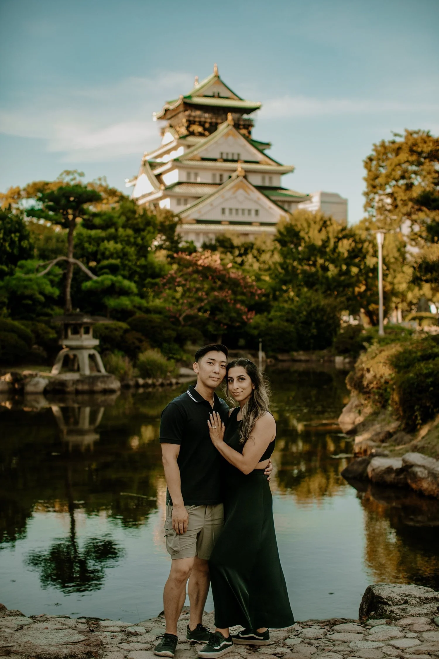 Couple standing together beside the moat with Osaka Castle reflected in the water behind them