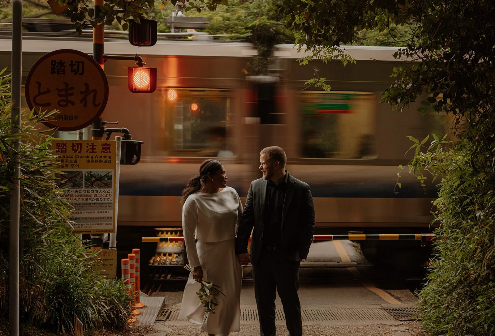 Bride and groom smile at each other beside the tracks as a train rushes by in Tokyo.