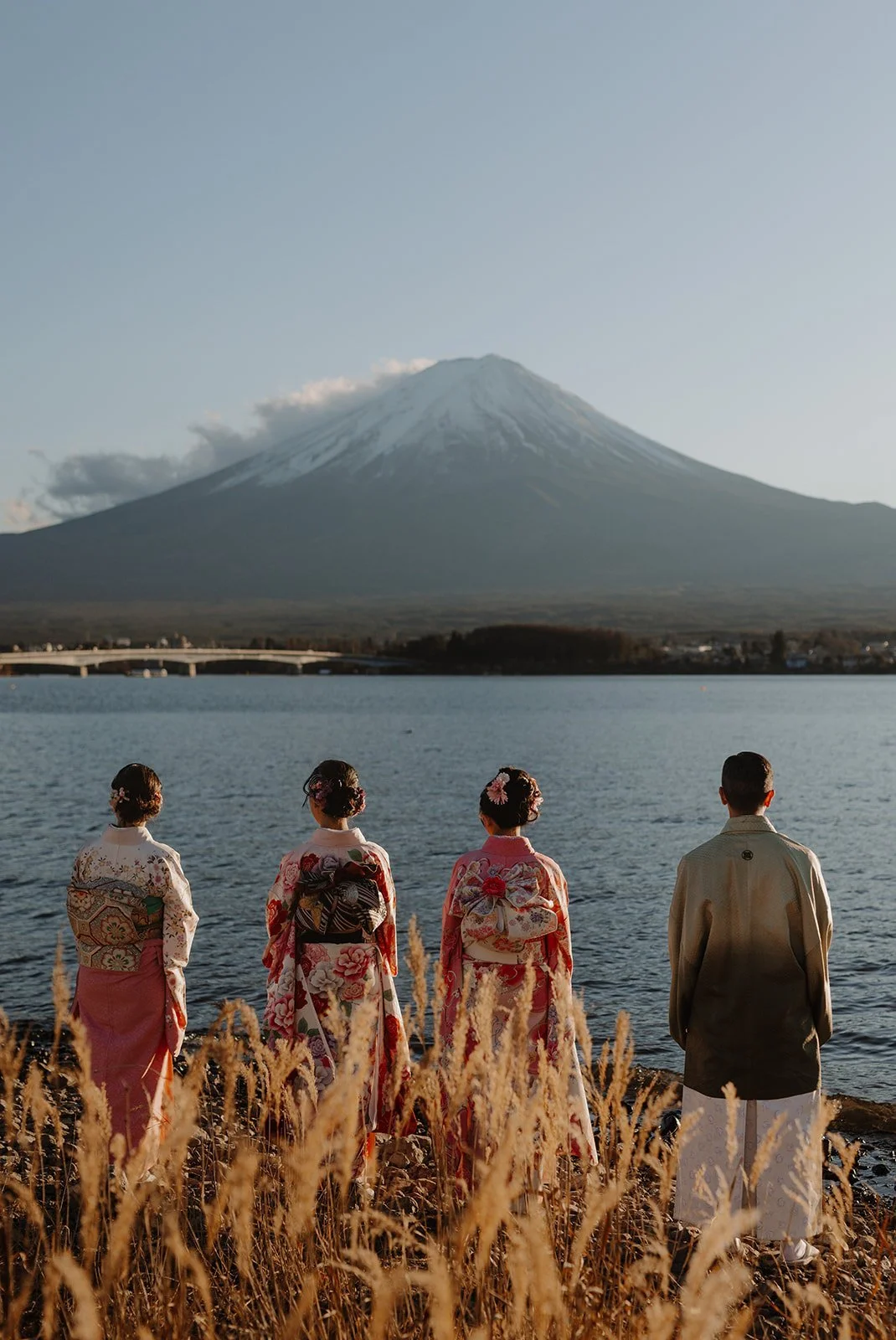 Family in traditional kimono standing on the shore of Lake Kawaguchiko facing snow-capped Mount Fuji