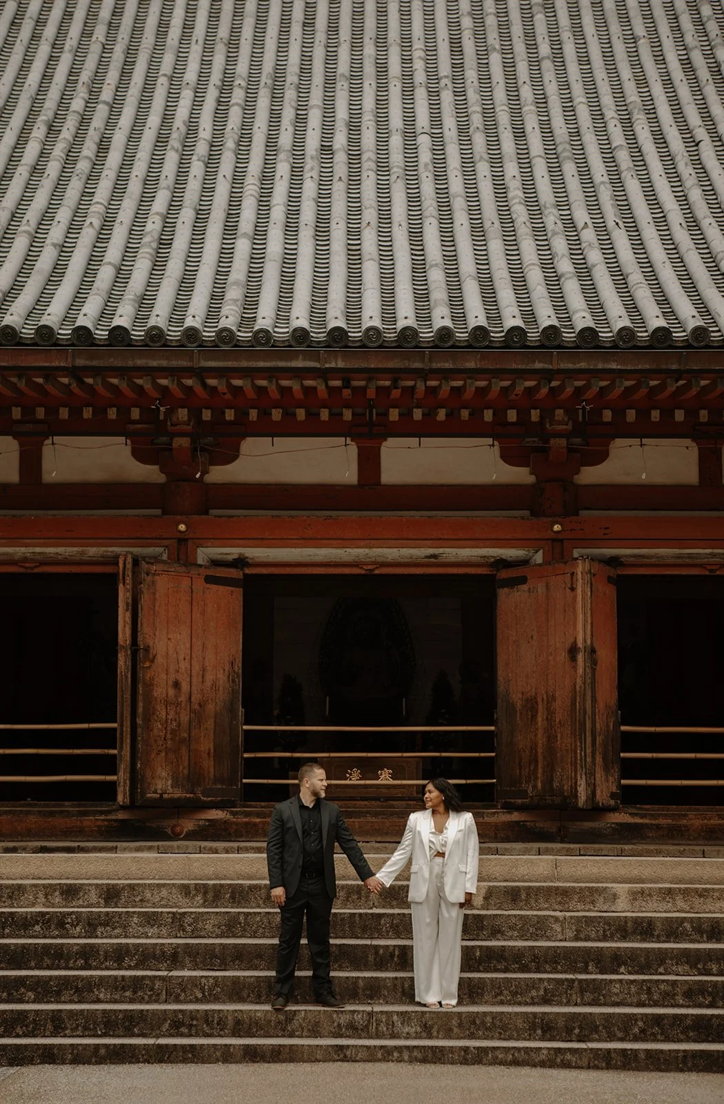 Bride and groom hold hands on the steps of Daigo-ji's main hall in Kyoto.
