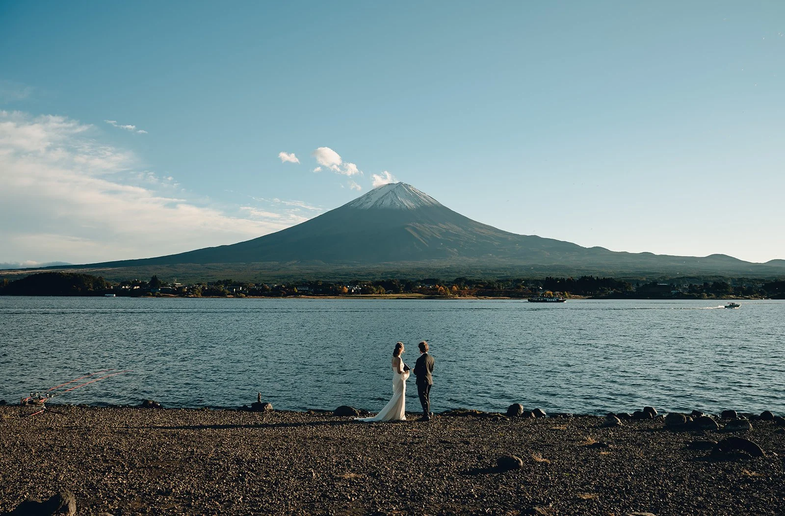 Bride and groom stand at the lake's edge exchanging vows with Mount Fuji visible across the water.