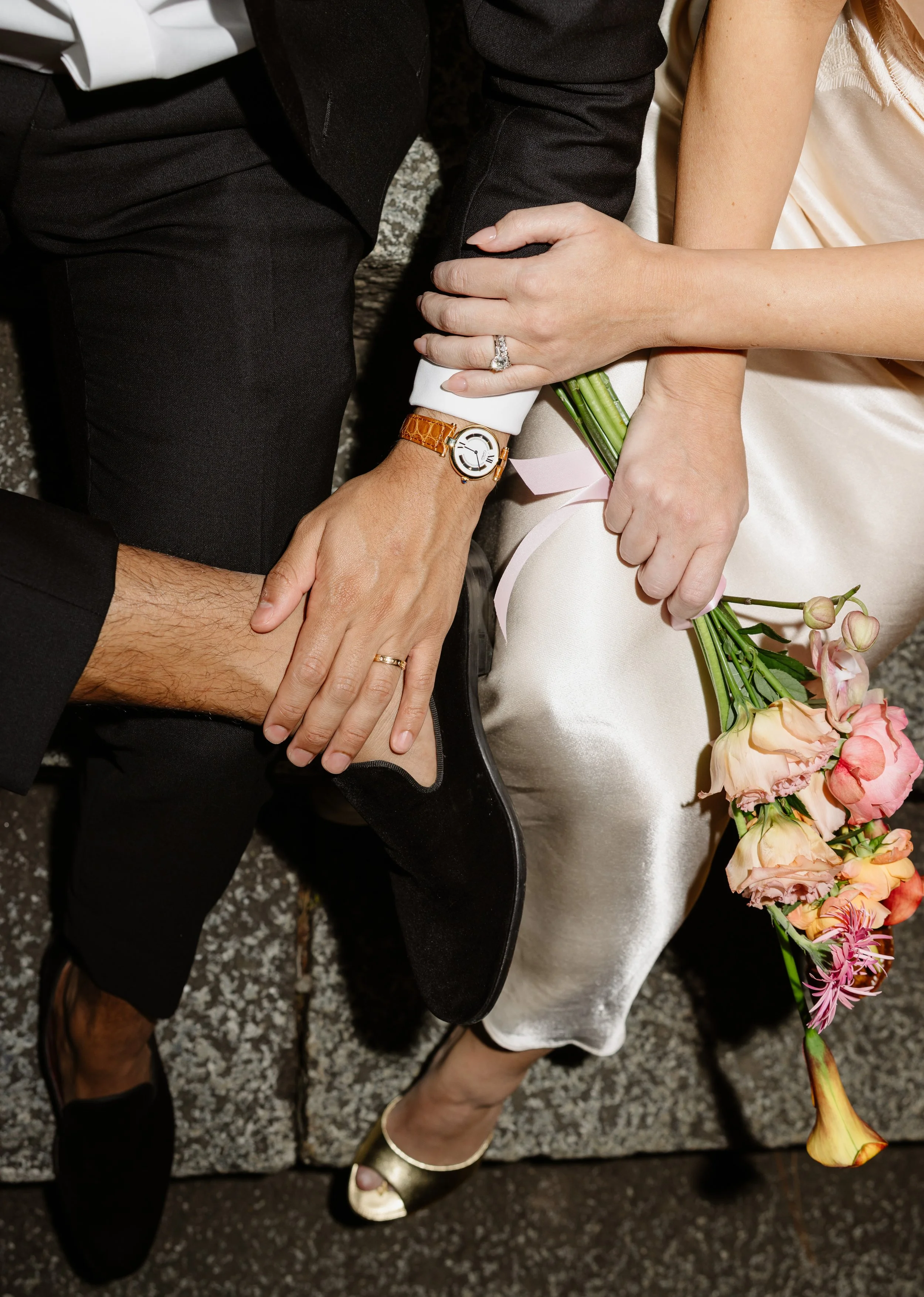 lose-up of a couple’s clasped hands with an engagement ring and gold wedding band, a pastel bouquet and gold heels, a Kyoto pre-wedding detail.