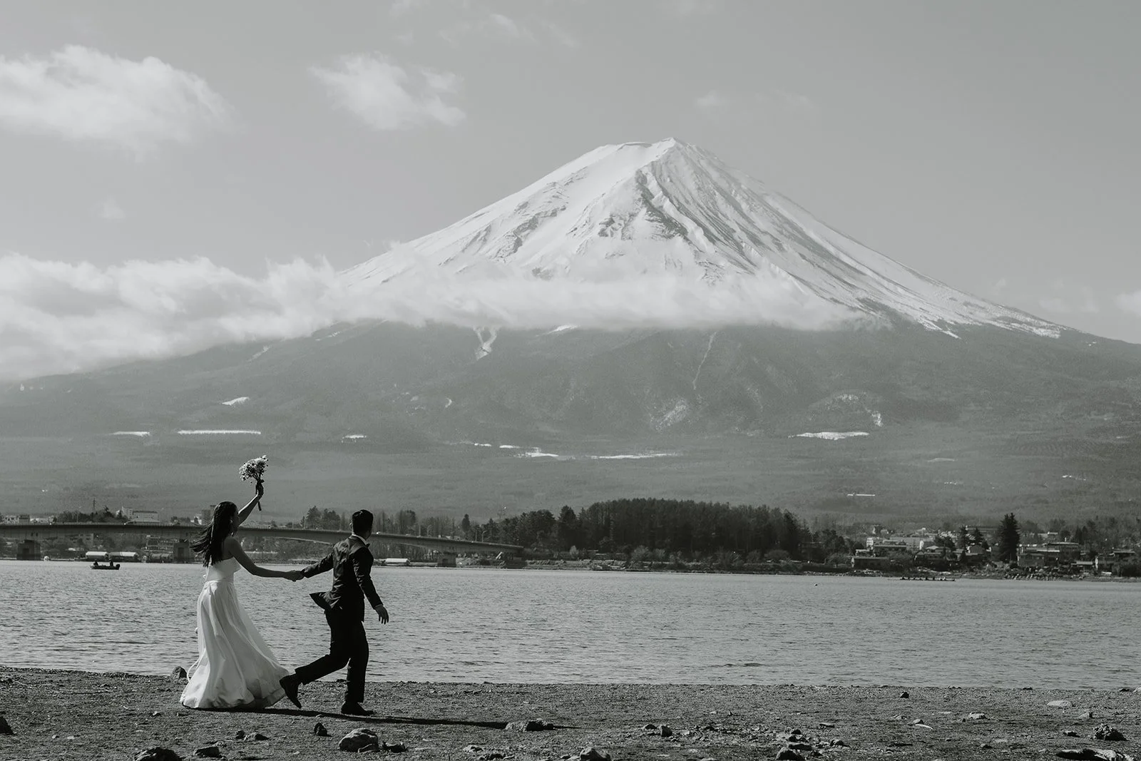Black and white version of the couple running joyfully along the shore with Mount Fuji behind them.