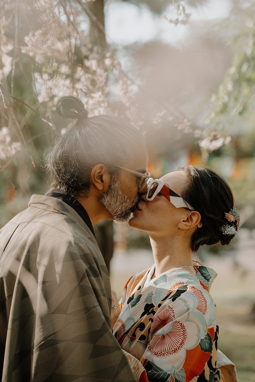 Couple in kimono kissing beneath cherry blossom trees in Kyoto, Japan