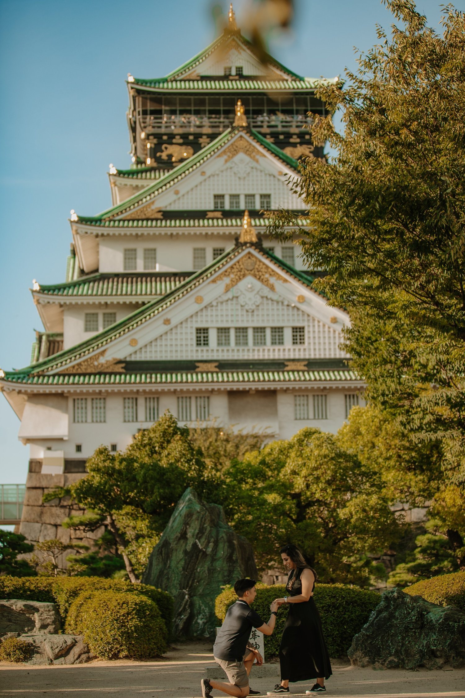 Man kneeling to propose with the main tower of Osaka Castle rising behind the couple