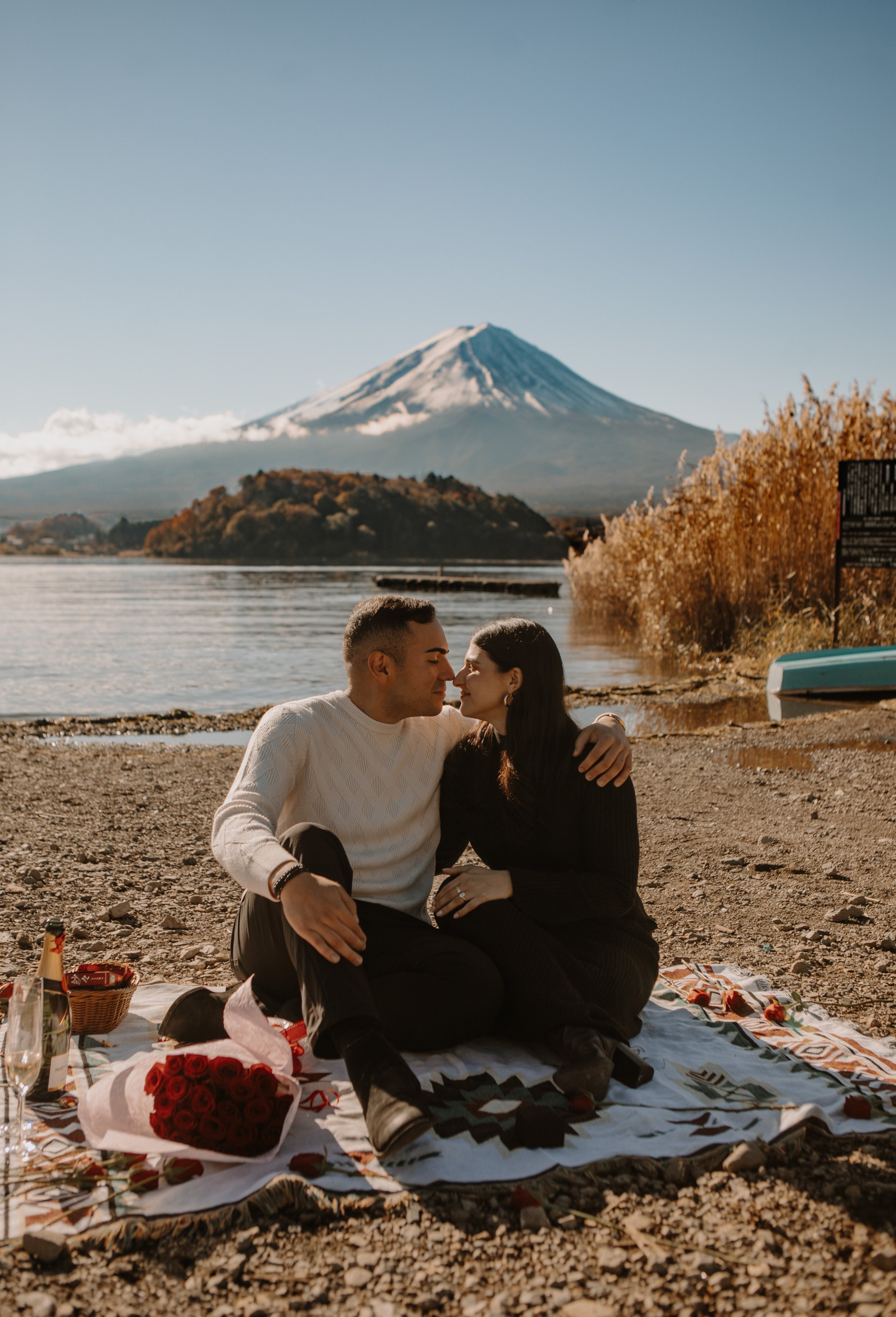 Newly engaged couple sharing a picnic with roses and champagne on the shore of a Mount Fuji lake