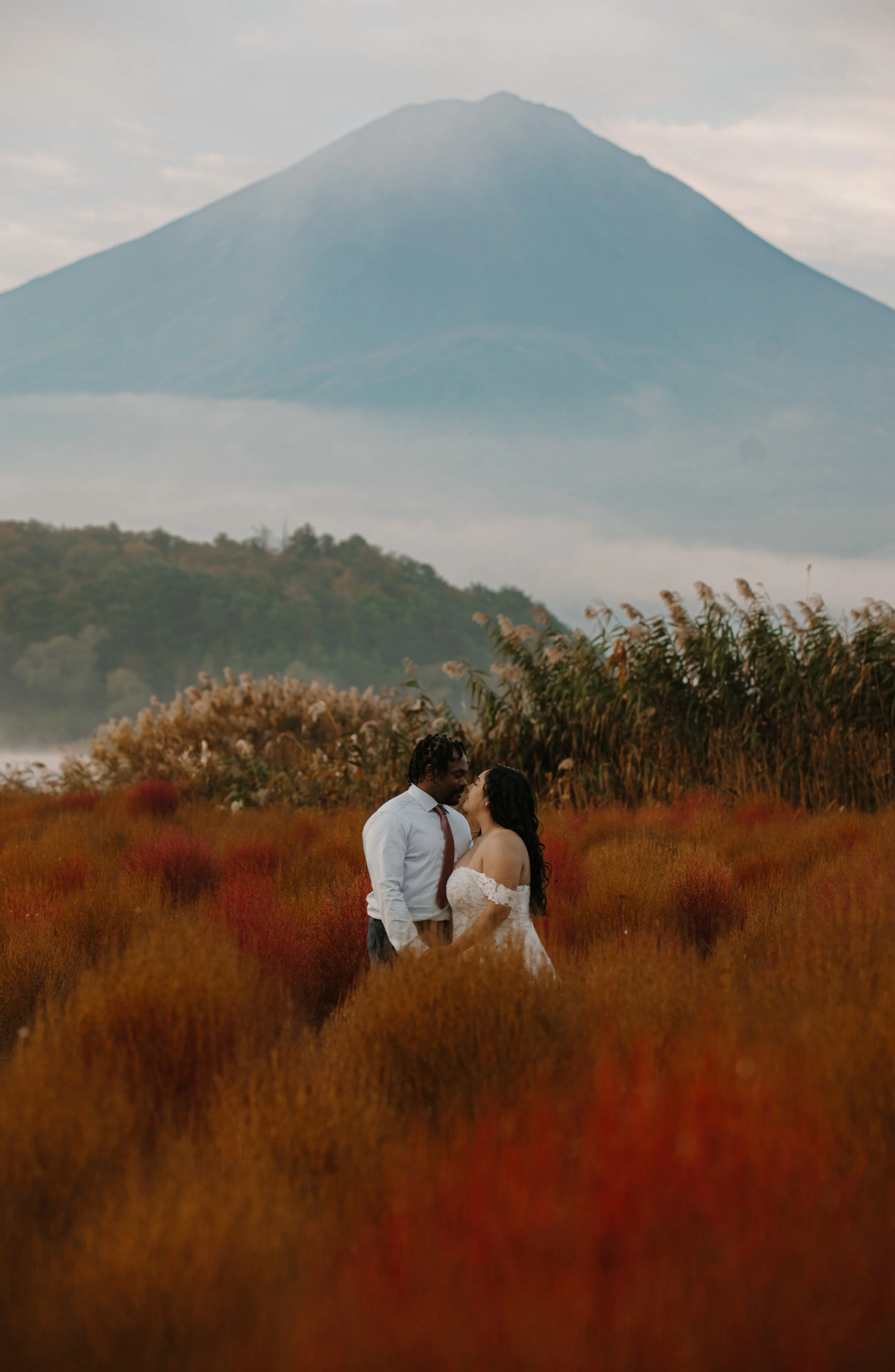 Bride and groom kissing in a red autumn field with Mount Fuji rising behind them