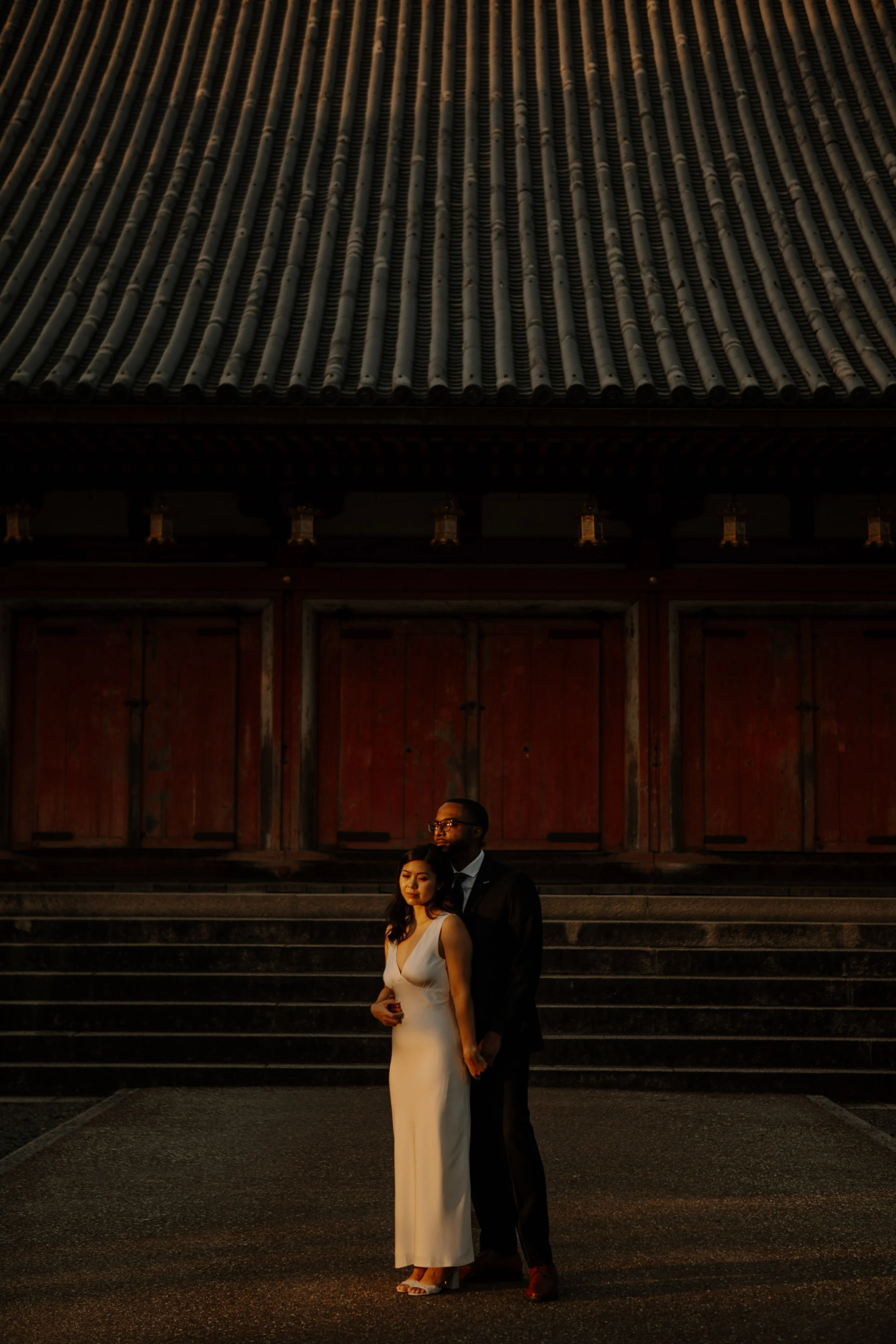 Couple embracing in golden evening light against the red doors and tiled roofline of Sensoji Temple in Asakusa, Tokyo.