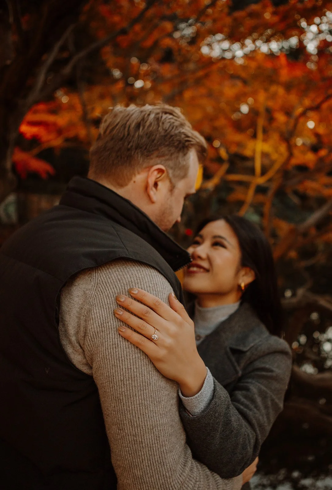 Close-up of a new engagement ring resting on a partner's shoulder against autumn leaves in Tokyo