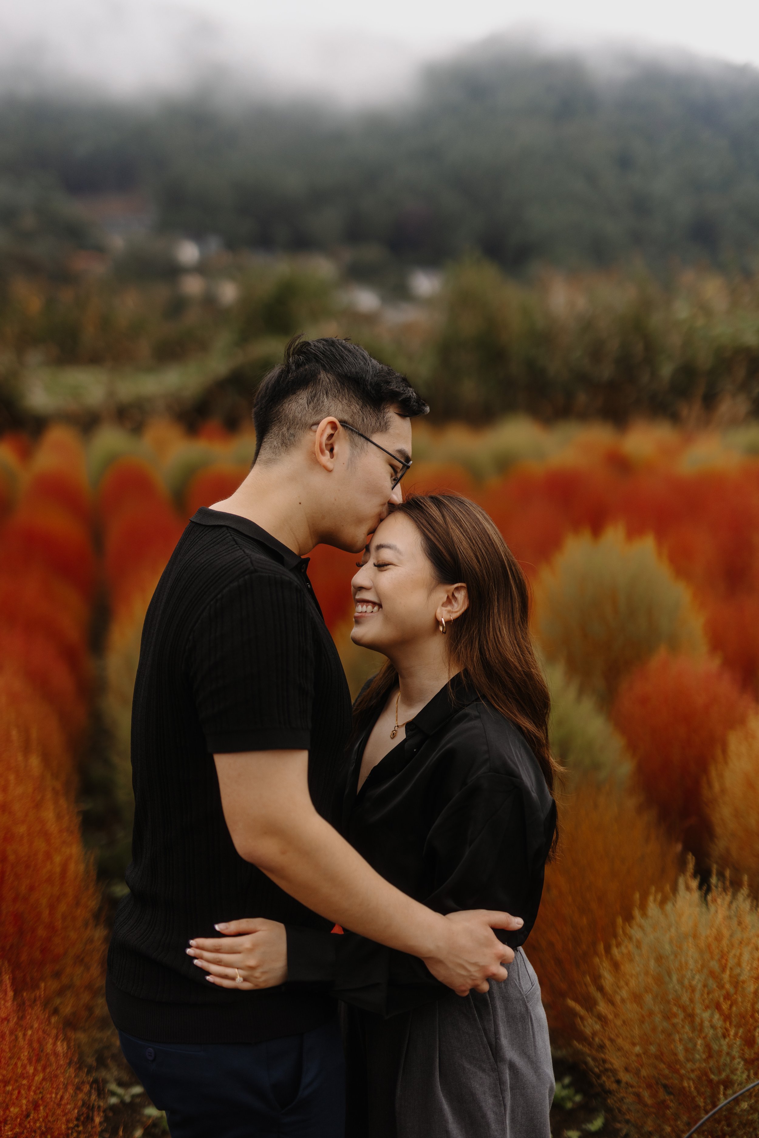 Couple embracing with a forehead kiss in a red kochia grass field on a foggy day