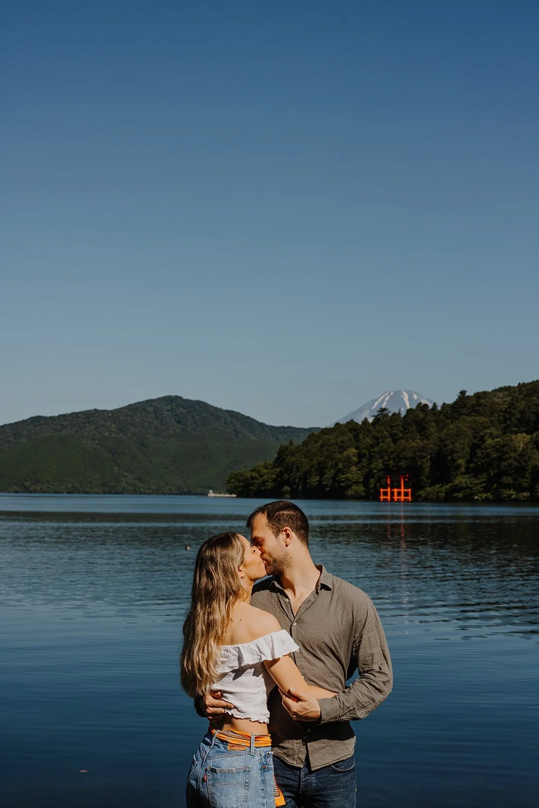 Couple sharing a kiss beside Lake Ashi with Mount Fuji rising behind them, Hakone engagement photography