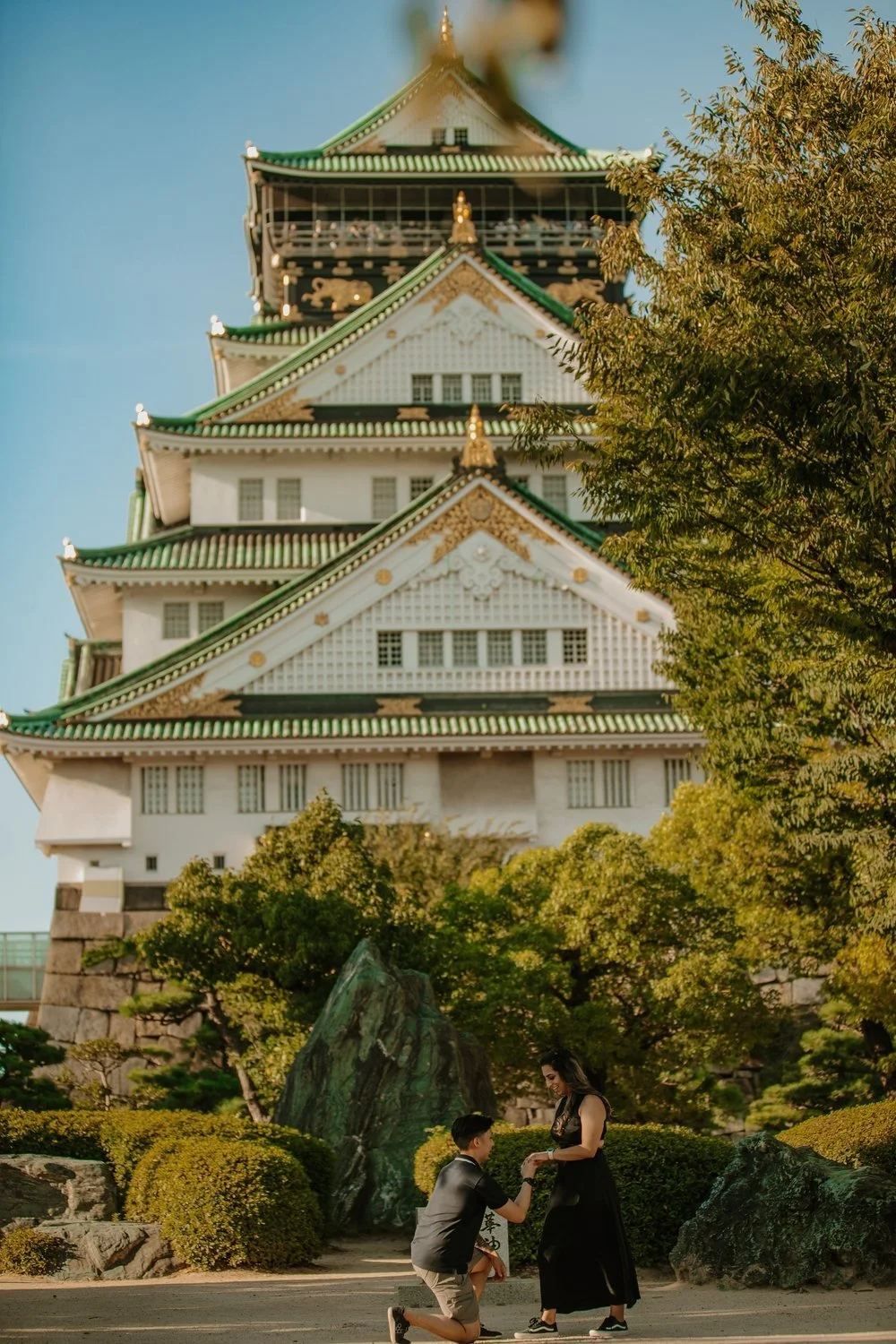 Man kneeling to propose with Osaka Castle's main tower rising behind the couple