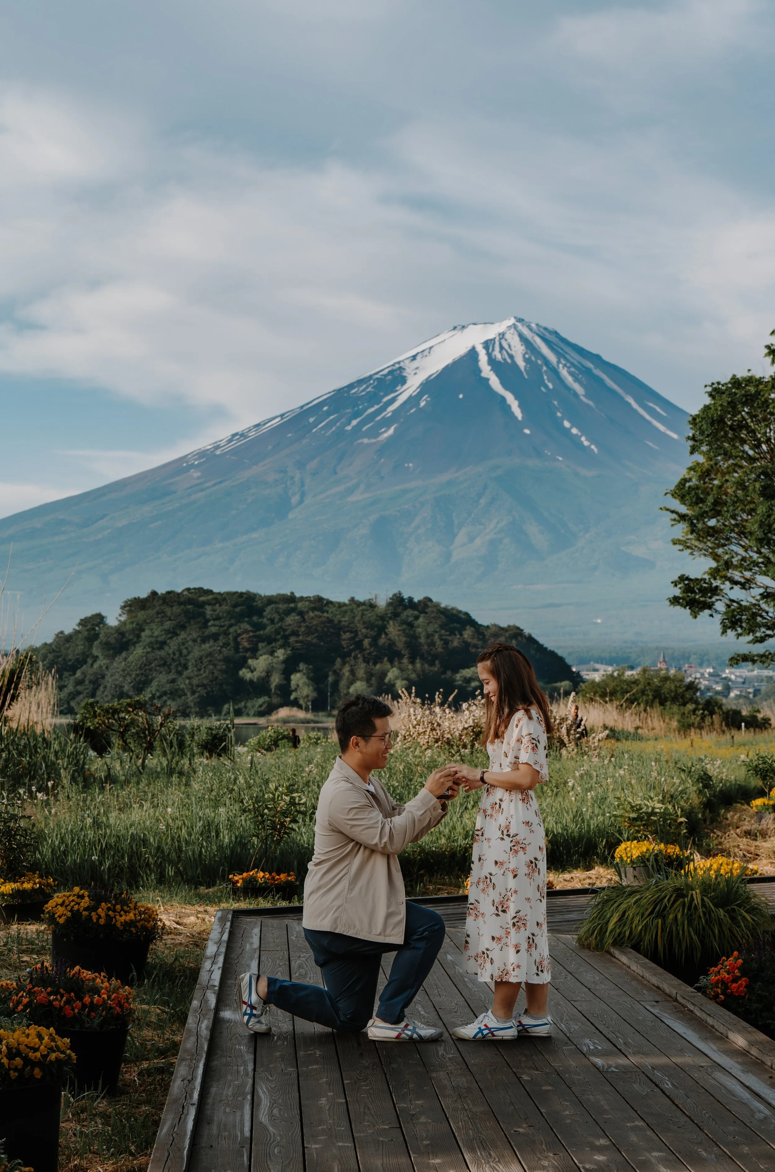 Man kneeling to propose on a wooden garden deck surrounded by flowers, Mount Fuji behind them