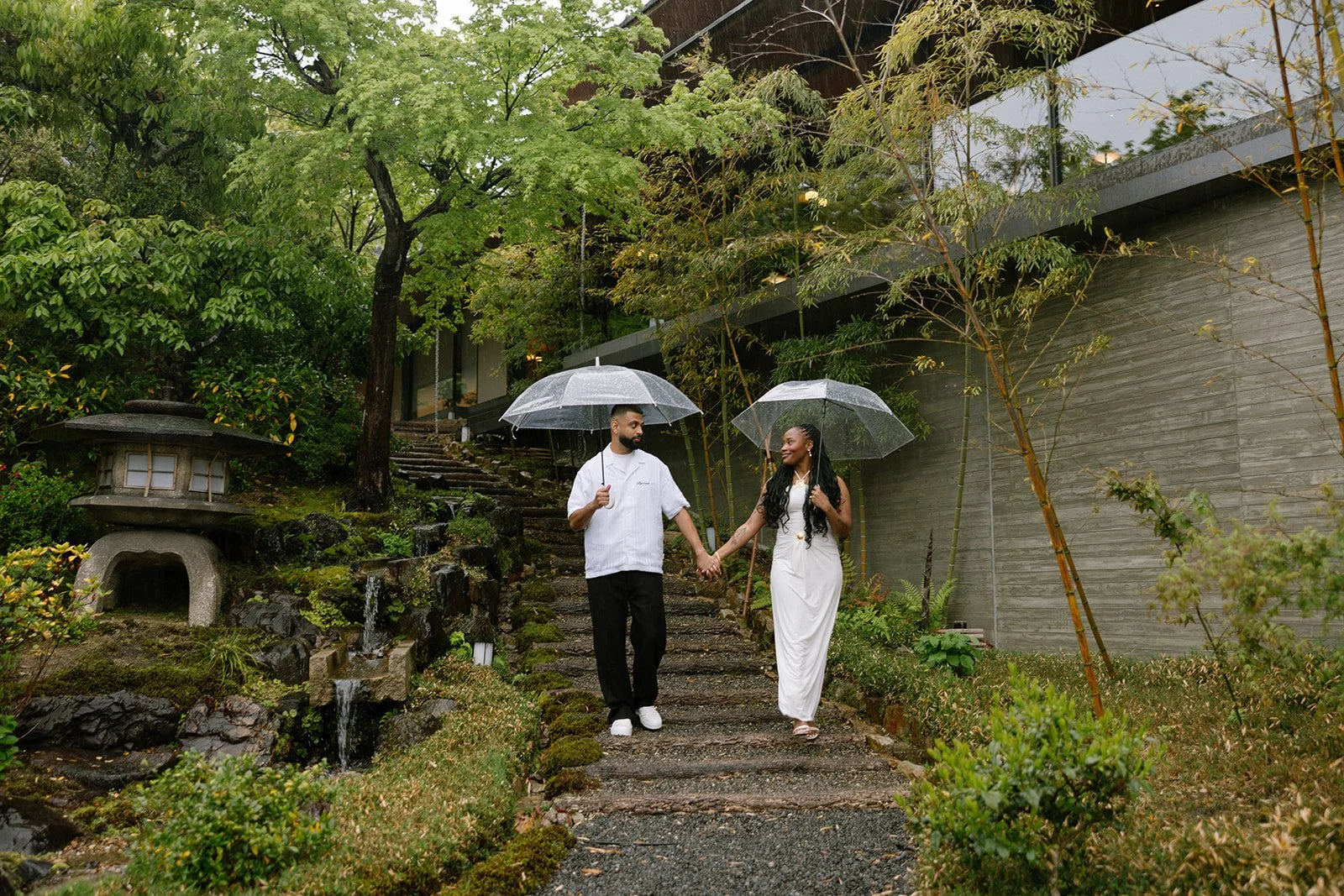Suhail and Thelma facing each other on a rain-soaked garden path at Park Hyatt Kyoto, umbrellas in hand