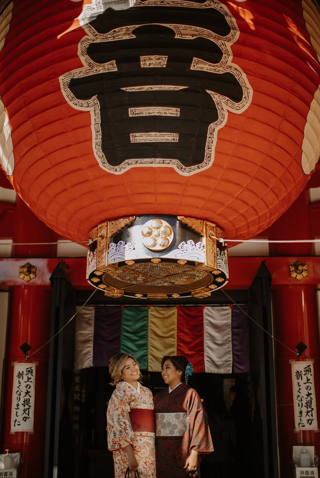 Two women in colorful kimono smiling beneath a giant red lantern at a temple gate in Asakusa, Tokyo