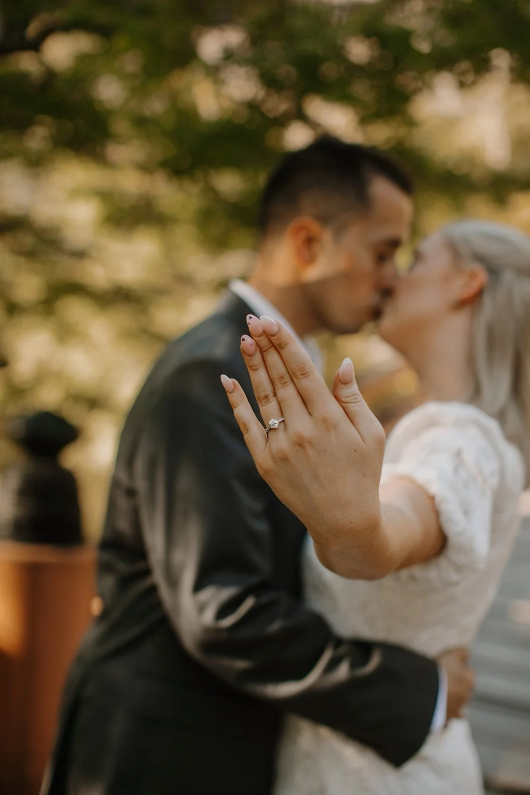 Client testimonial photo of a couple kissing outdoors, close-up on the bride's engagement ring