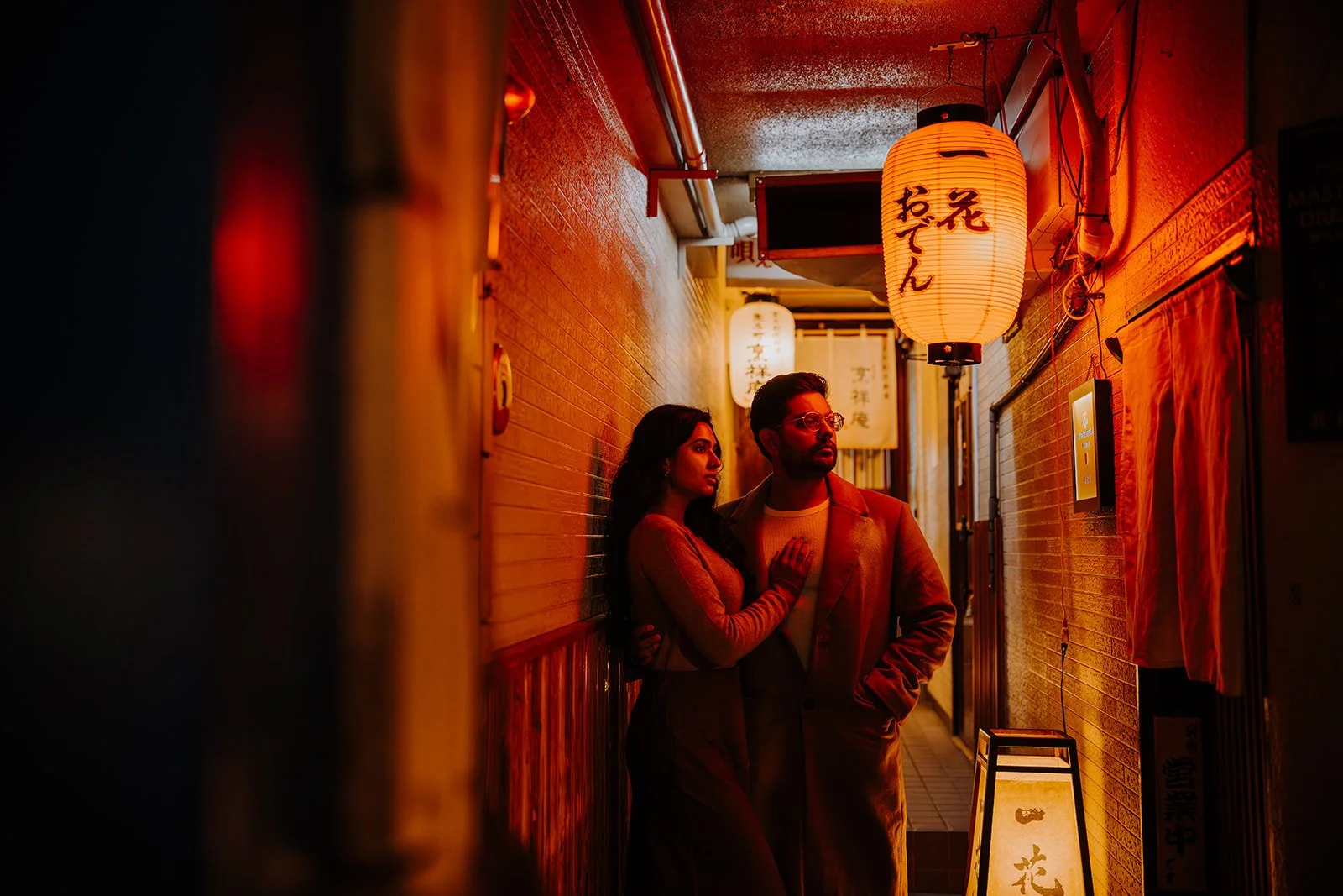 Avanika and Parichay stand in a narrow backstreet lit by a glowing red paper lantern in Japan
