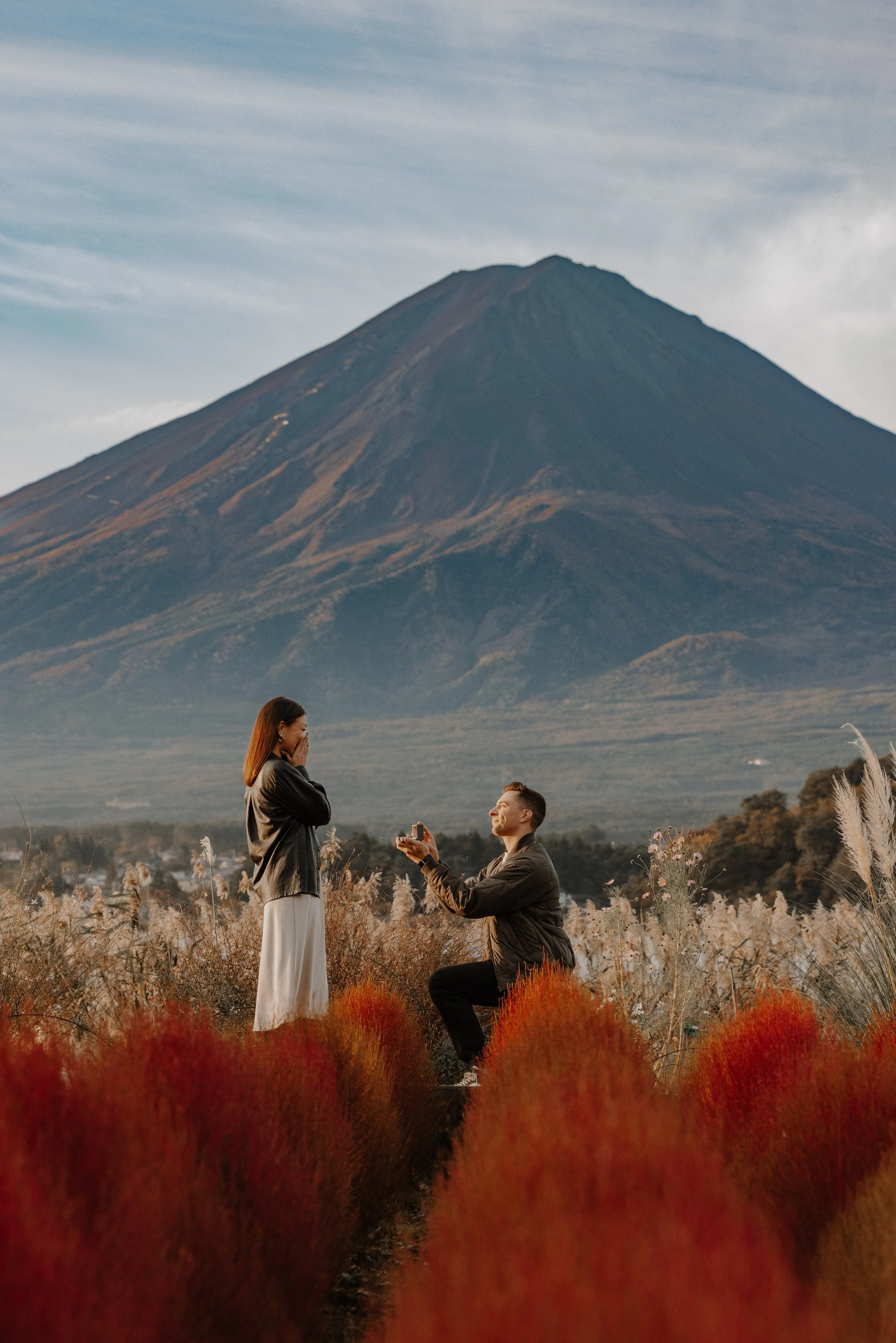 Man kneeling to propose in a field of red kochia grass with Mount Fuji rising behind him
