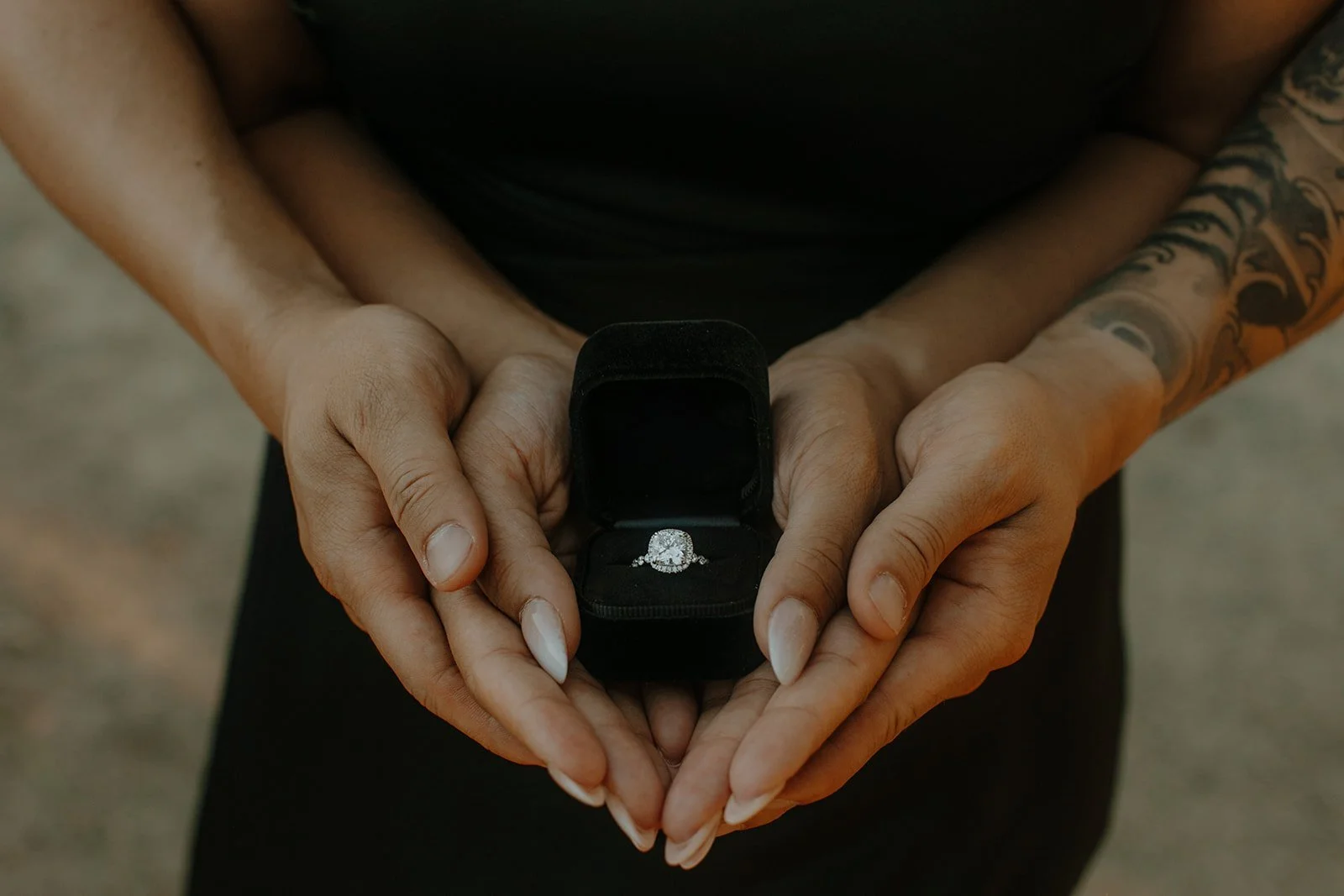 Close-up of a woman's hands cupping an open ring box with a diamond engagement ring inside
