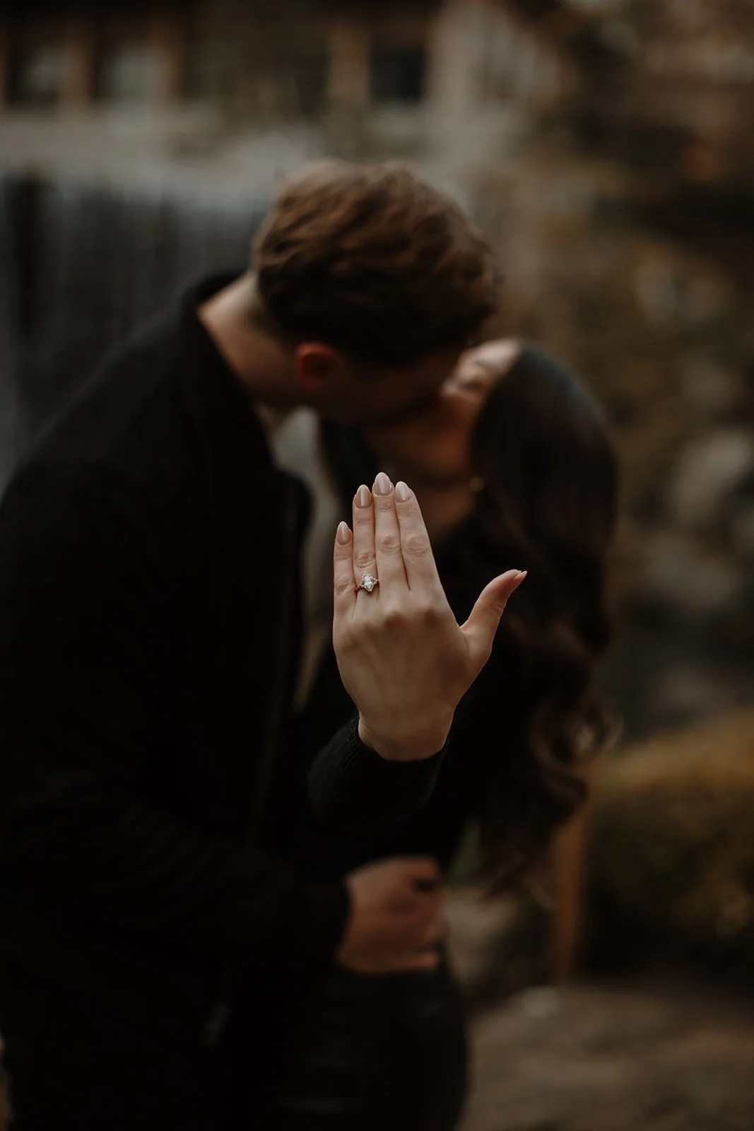 Couple's hands cupped in a heart shape holding a marquise diamond engagement ring in a teal velvet box.