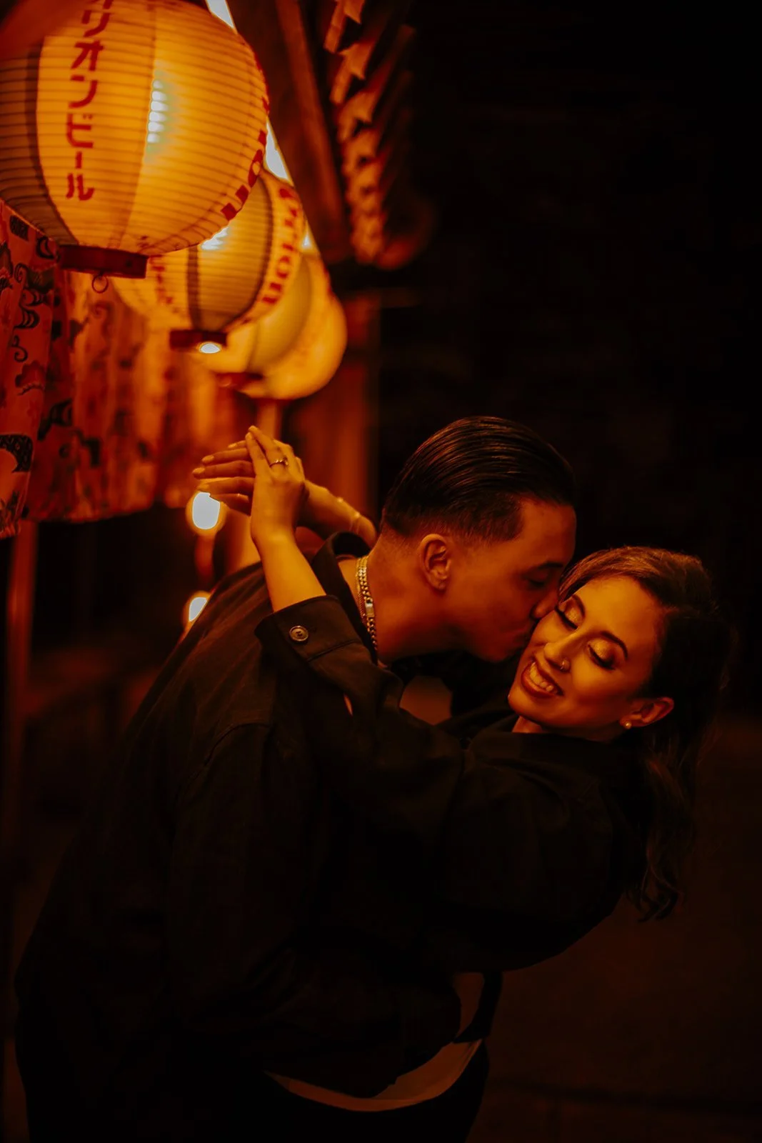Groom dipping his partner for a kiss beneath yellow paper lanterns in a Tokyo lantern-lit alley.