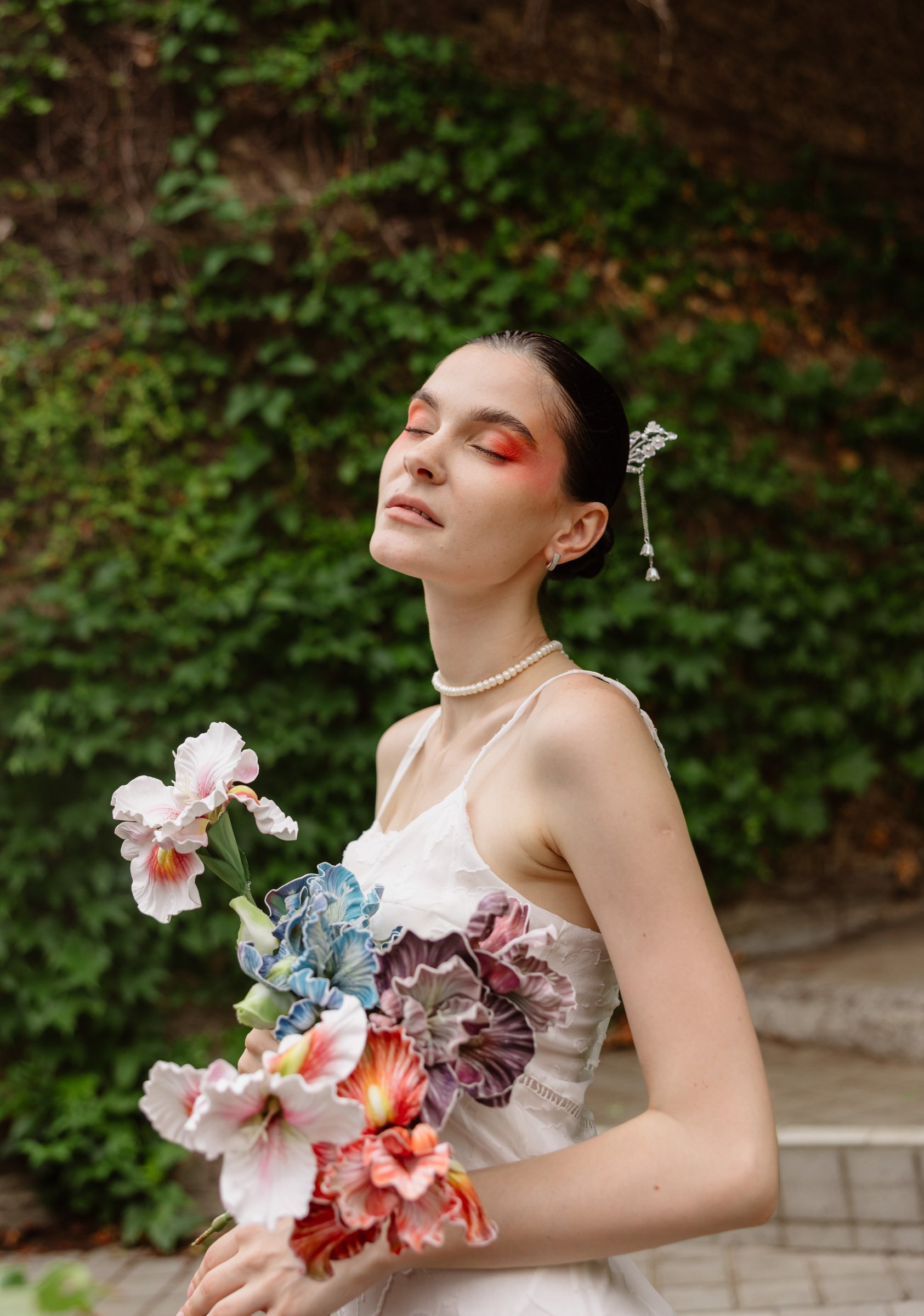 Editorial pre-wedding portrait of a bride with bold red eye makeup holding a sculptural floral bouquet