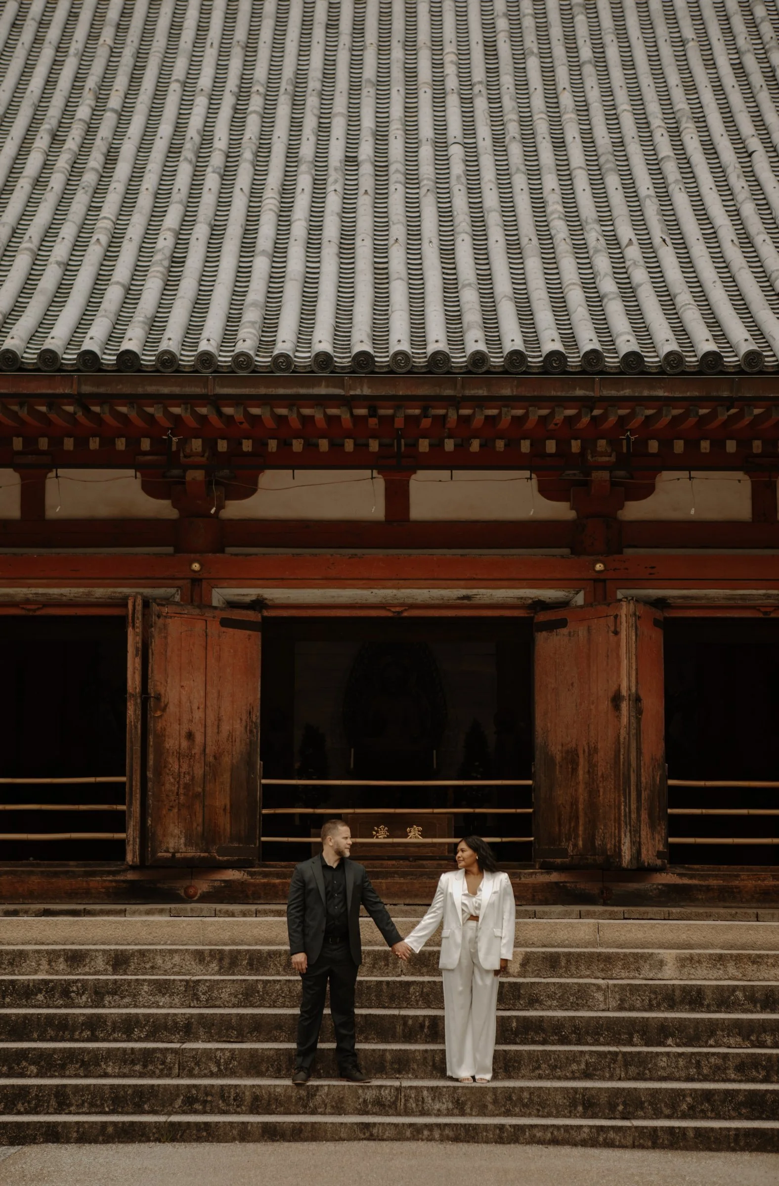 Couple in white and black outfits holding hands on the stone steps of a Japanese temple hall