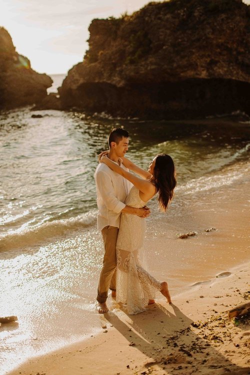 Couple embracing on an Okinawa beach cove at golden hour, surrounded by dramatic rock formations