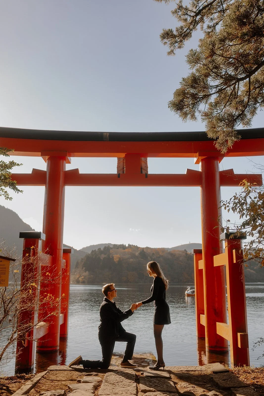 Man kneeling to propose beneath the red torii gate on Lake Ashi at Hakone Shrine