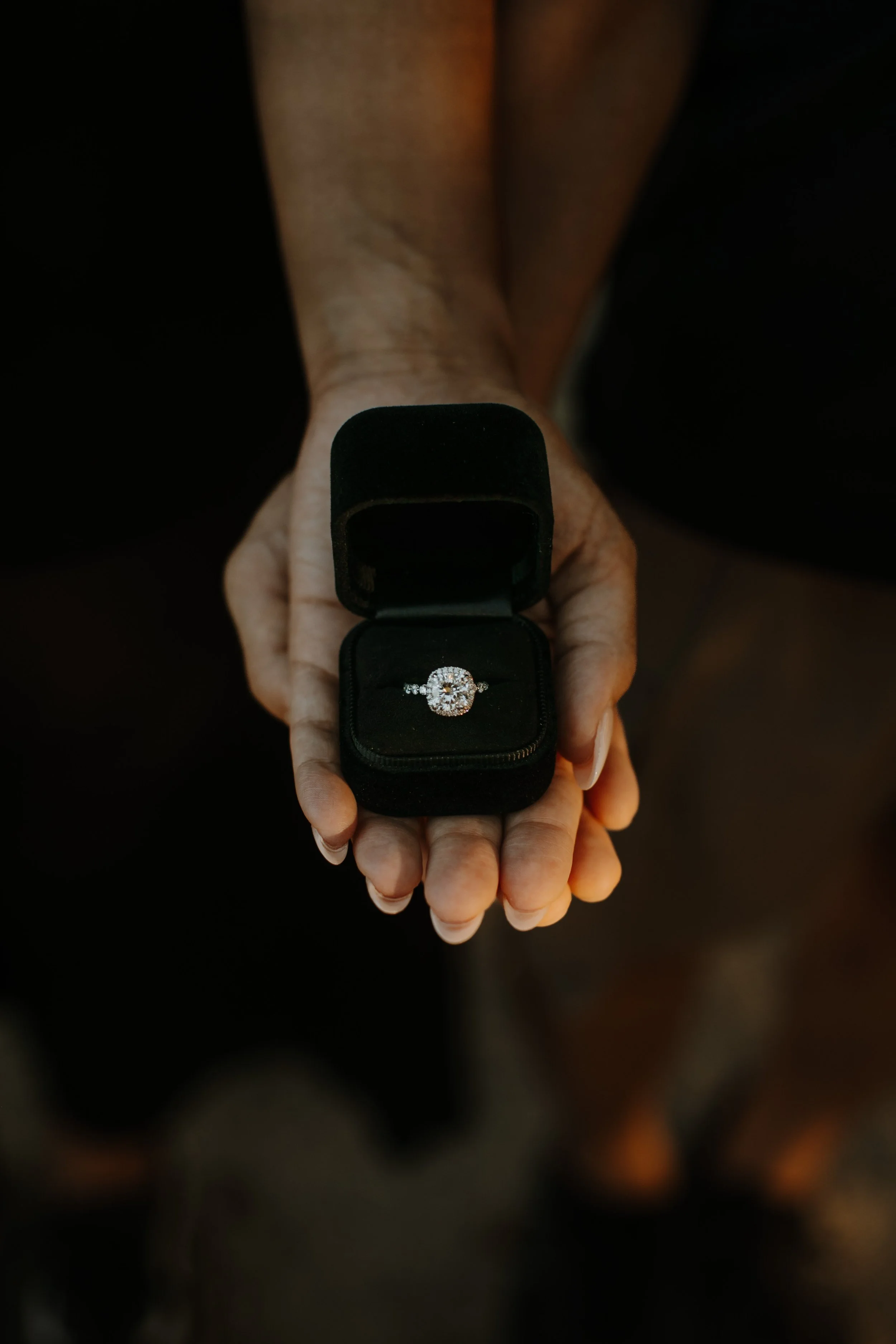 Close-up of a hand presenting an open ring box with a diamond engagement ring