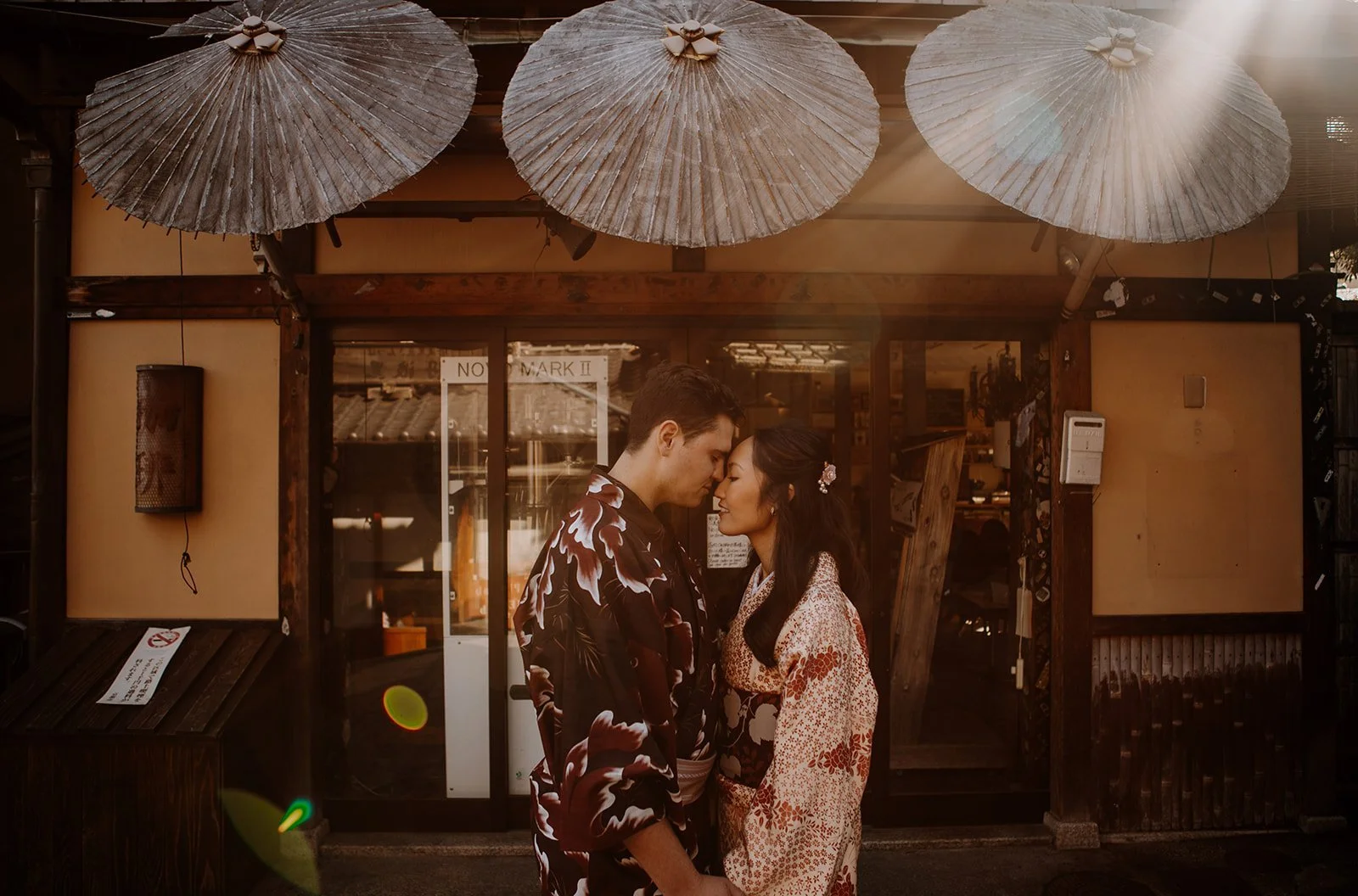 Couple in kimono embracing beneath traditional paper umbrellas on a historic street in Kyoto's Gion district