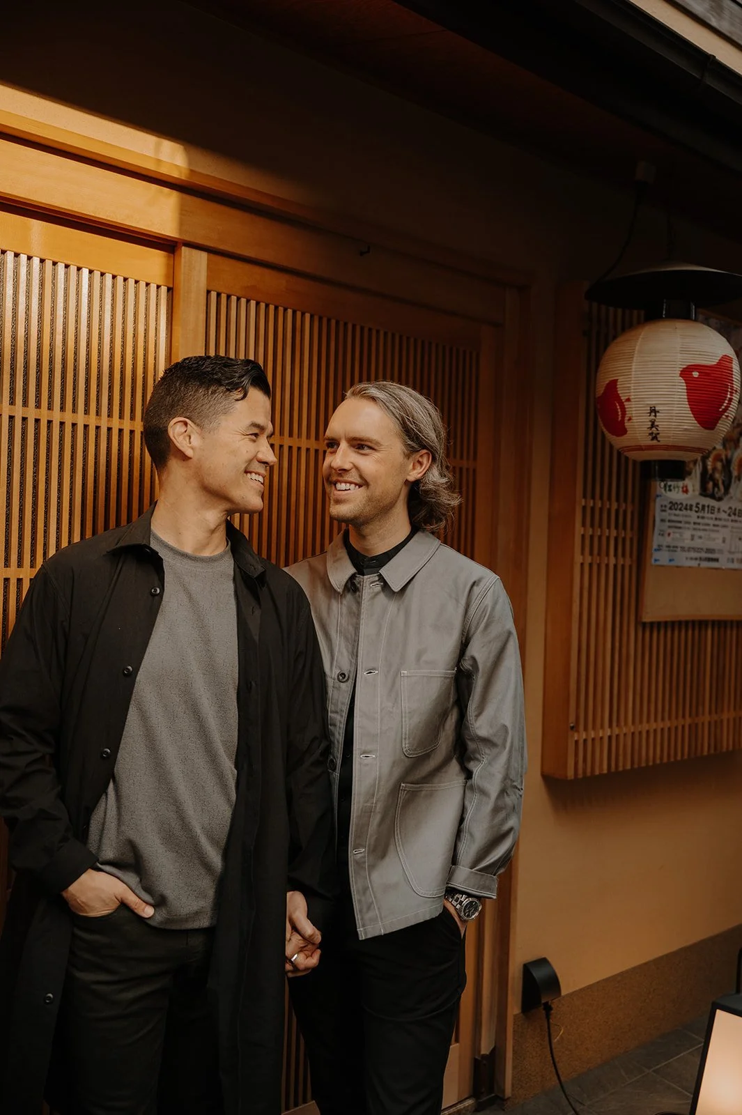 Same-sex couple smiling together in a lantern-lit Kyoto alley at golden hour