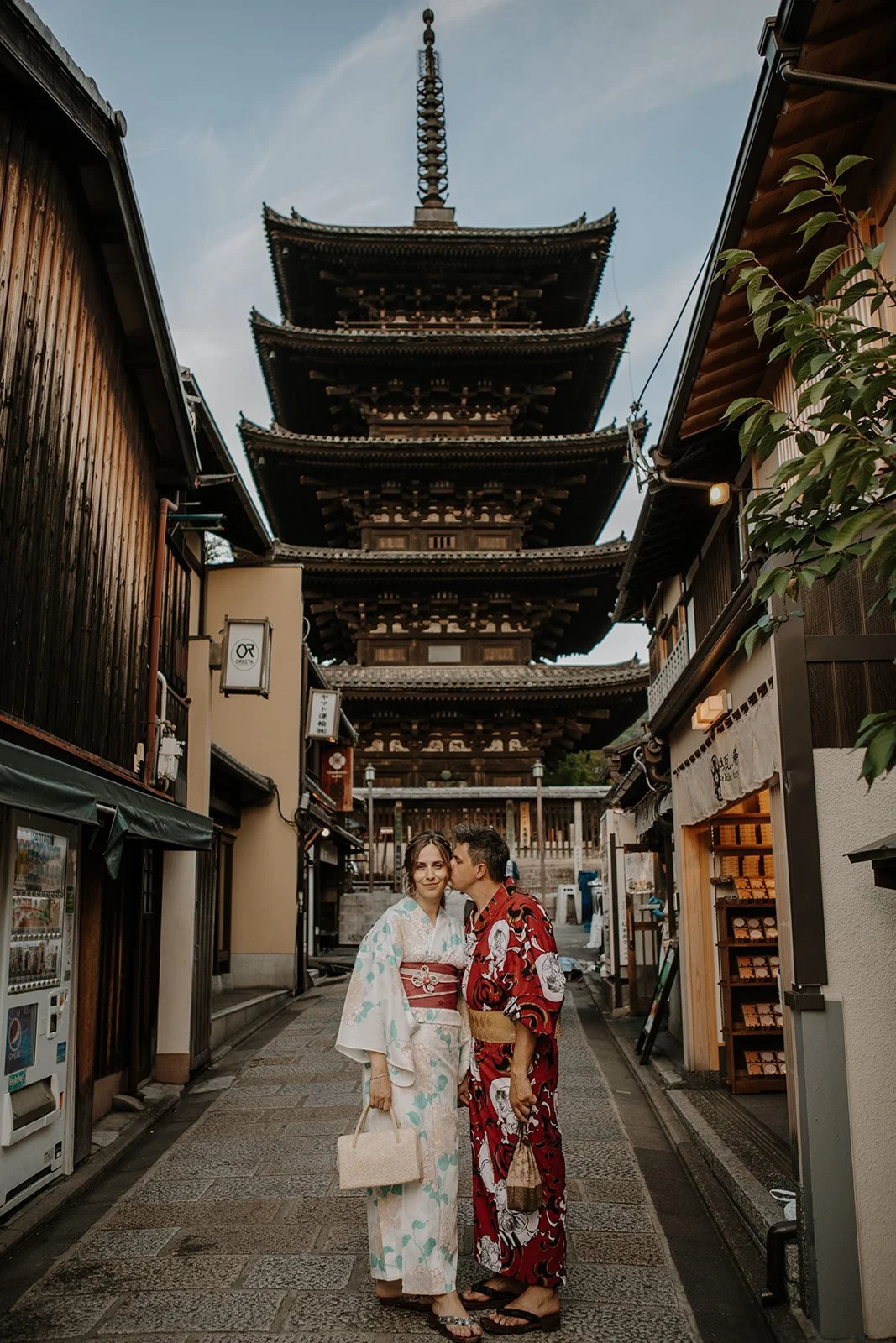 Couple in kimono sharing a kiss on a historic street with Yasaka Pagoda rising behind them in Kyoto