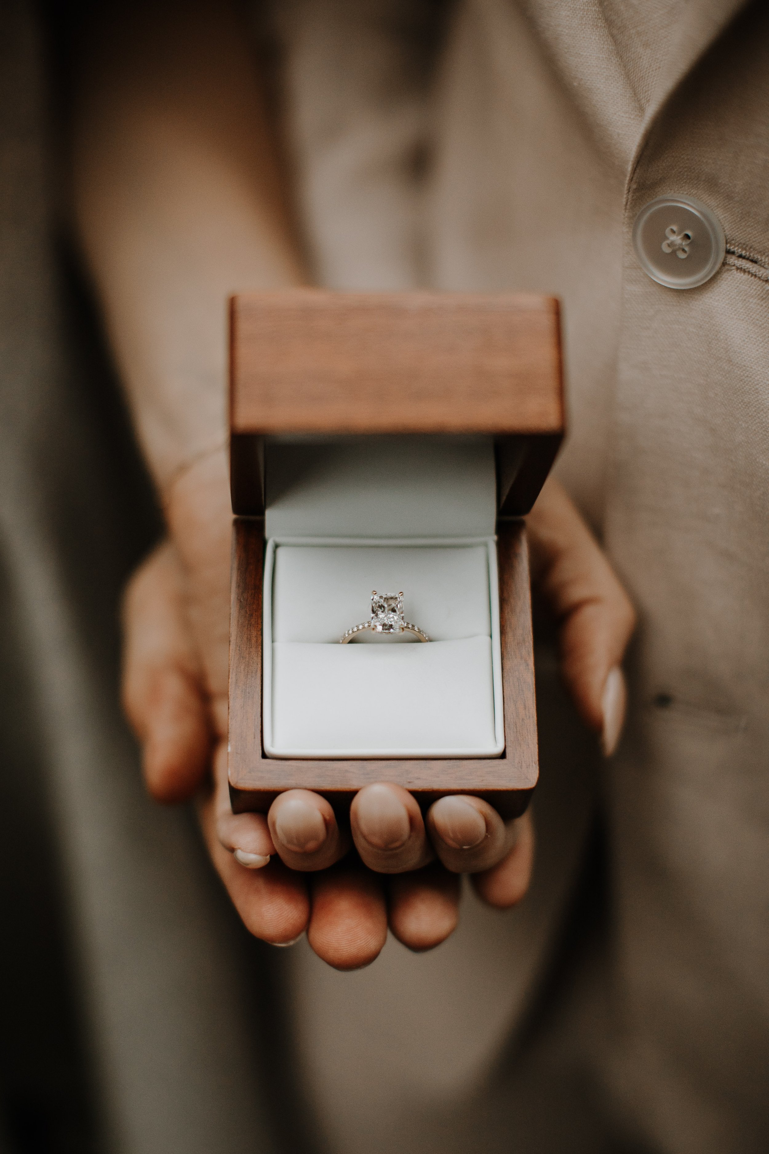 Close-up of a cushion-cut diamond engagement ring in a wooden ring box held by the groom