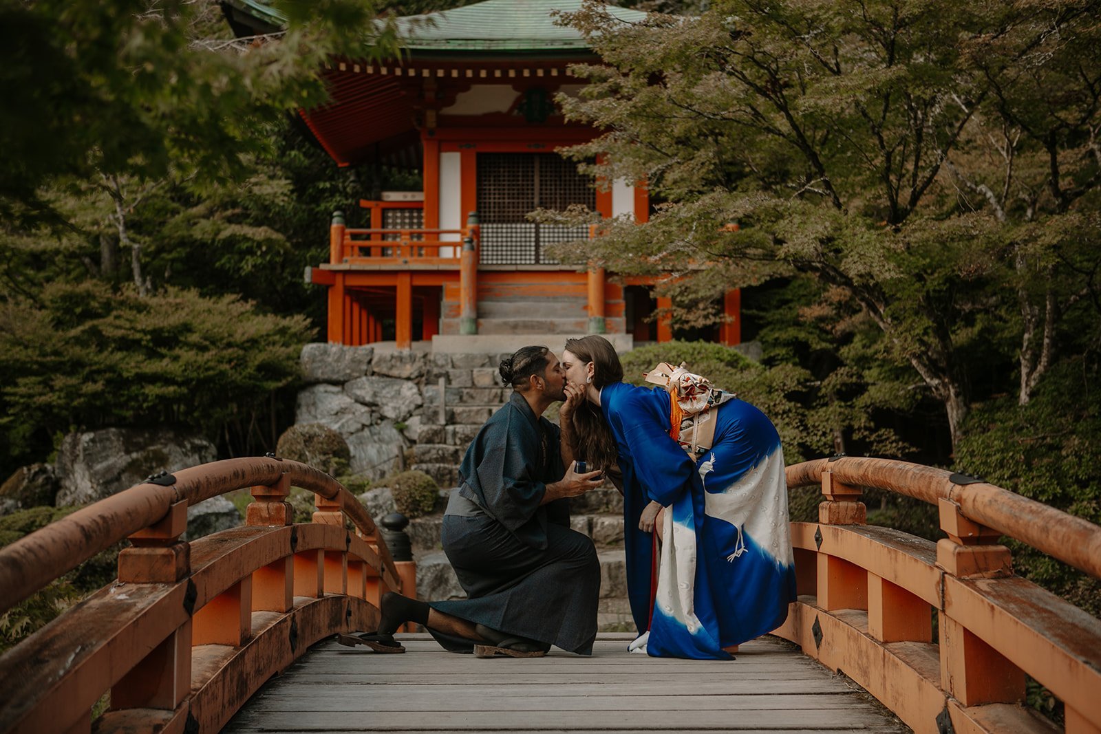 Close-up of a couple in formal kimono kissing on a vermilion bridge before a Kyoto temple pavilion
