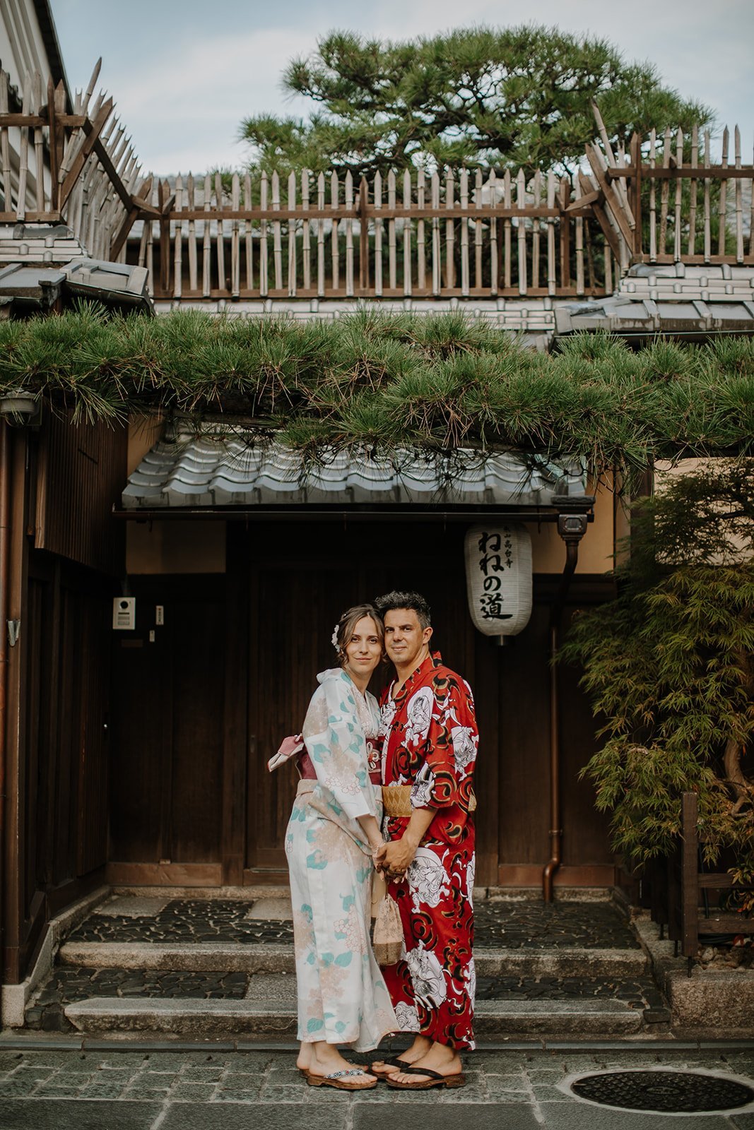 Couple in kimono standing arm in arm outside a traditional wooden building on Nene no Michi in Kyoto