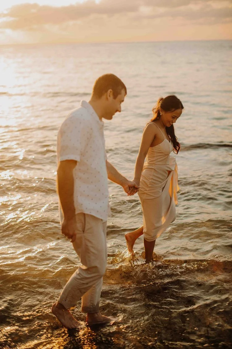 Couple holding hands and walking through shallow ocean water in Okinawa at sunset