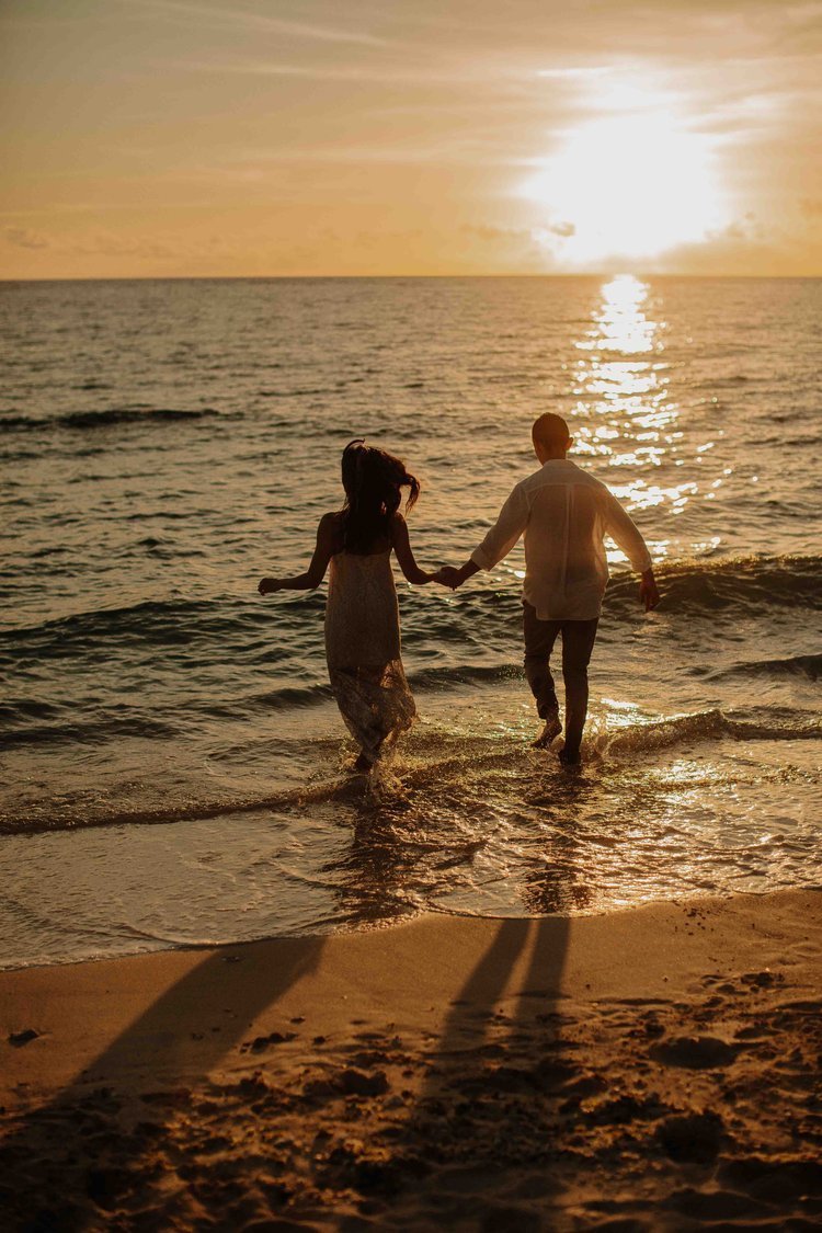 Silhouette of a couple holding hands and running into the waves on an Okinawa beach at sunset