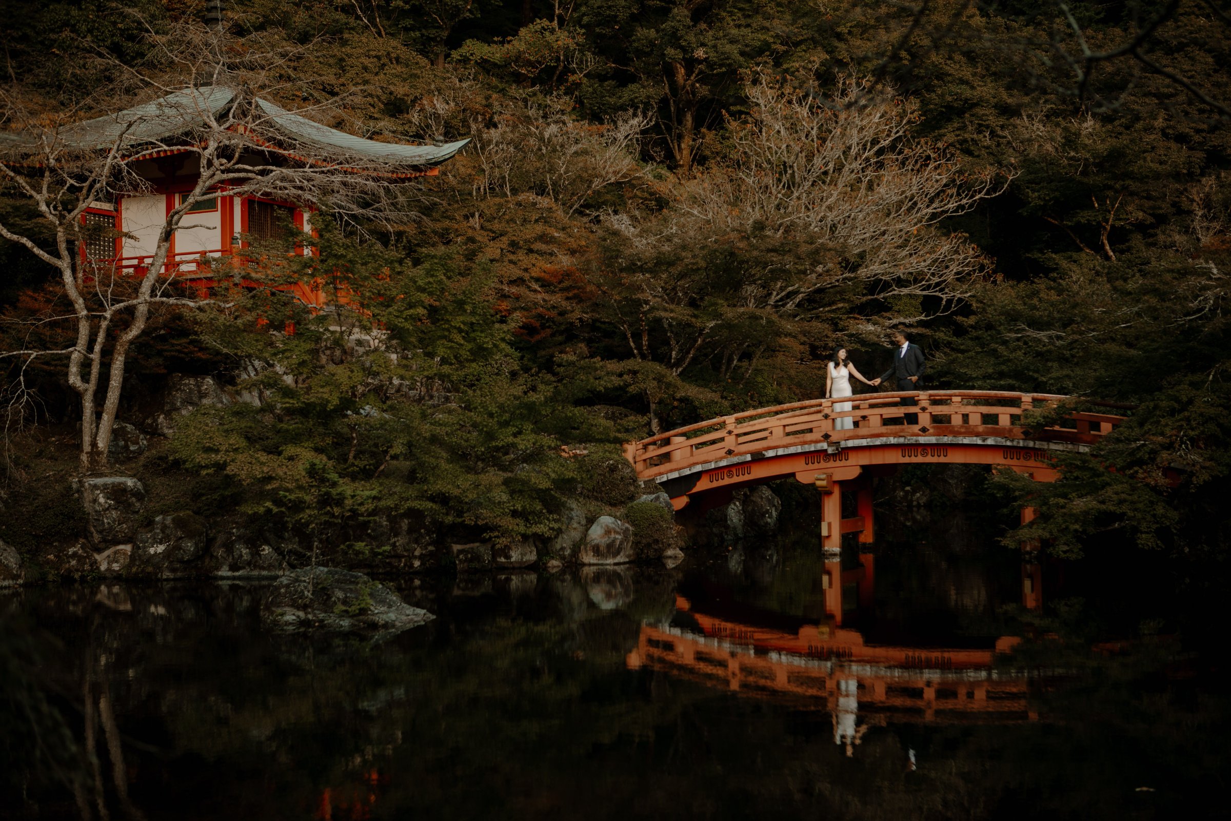 Pre-wedding couple on a red arched bridge reflected in the pond at Daigo-ji temple in Kyoto, Japan