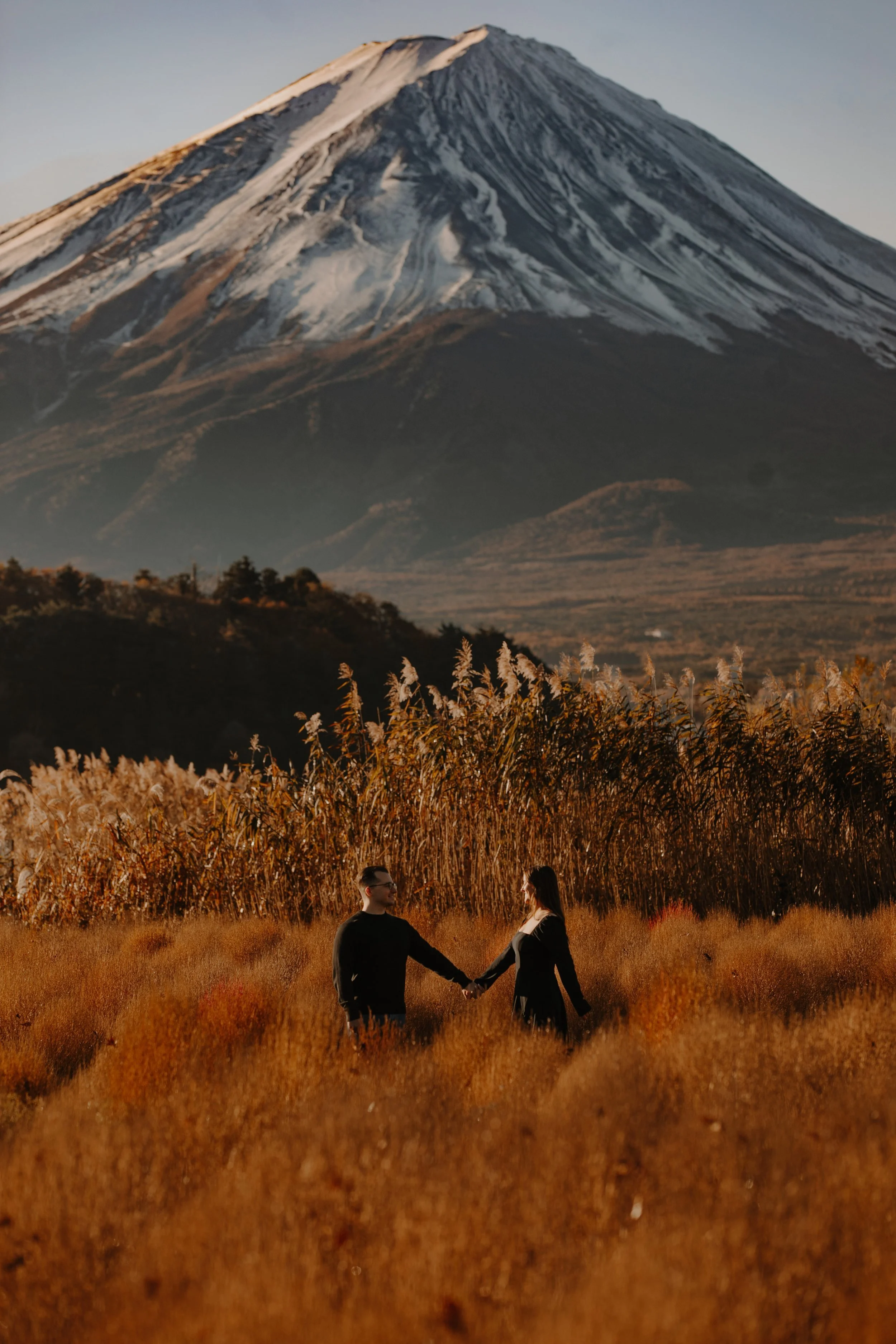 Client testimonial photo of a couple holding hands in an autumn grass field with Mount Fuji in the background