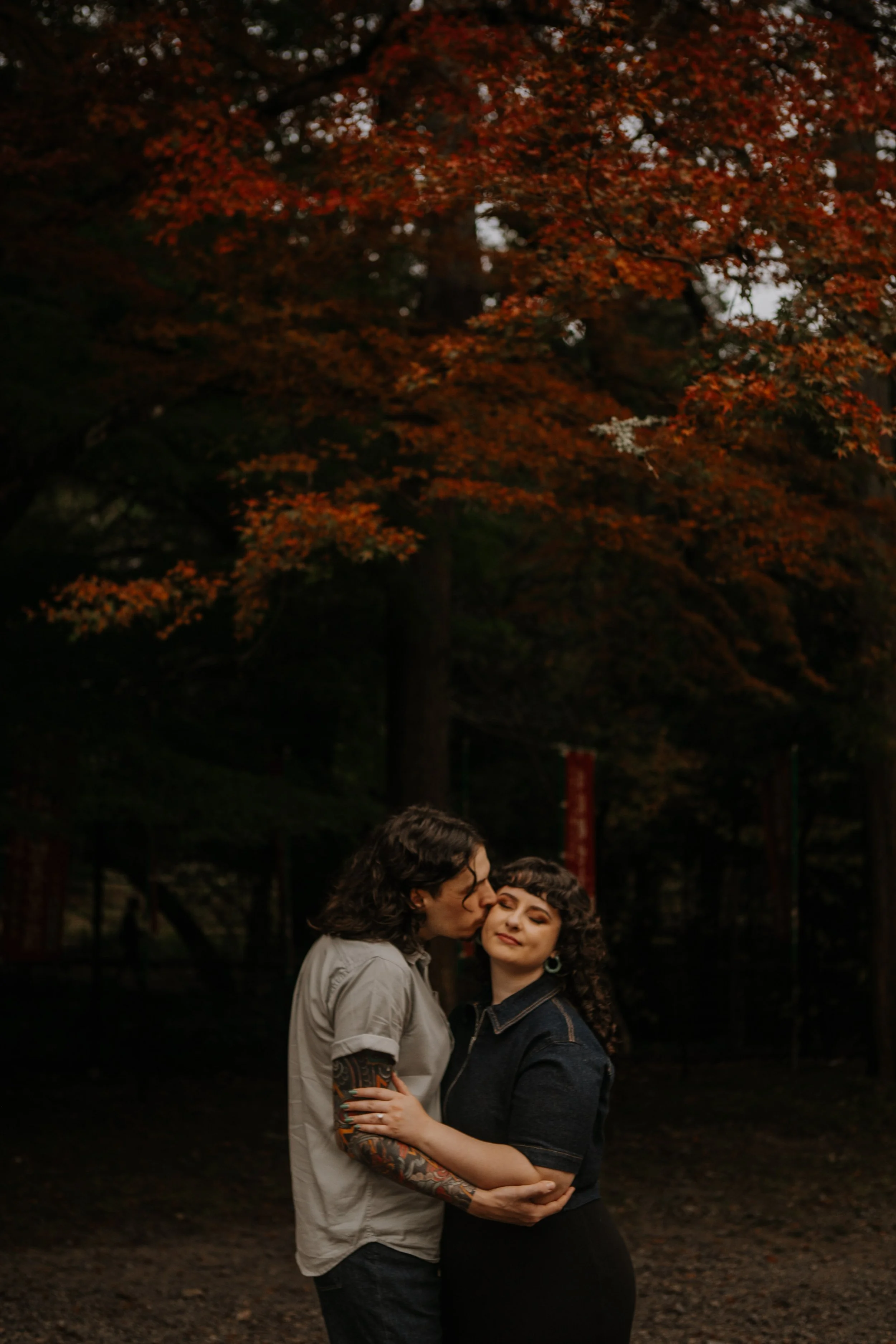 Couple sharing a cheek kiss beneath autumn maple leaves in a Kyoto garden